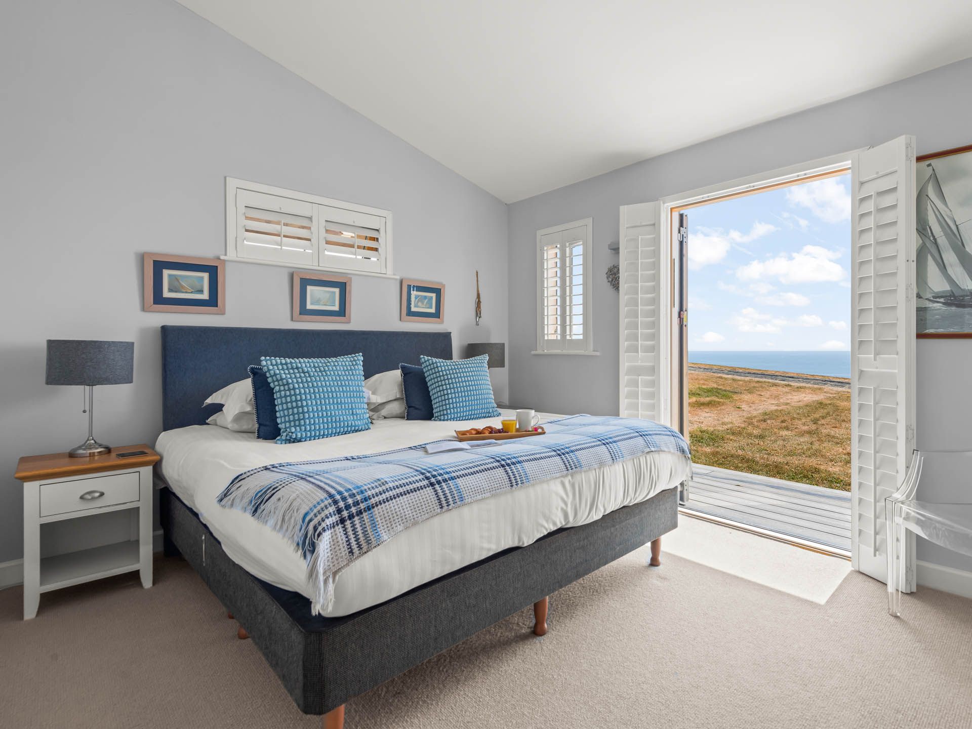 Bright coastal bedroom with double bed, blue cushions and open shutters overlooking the sea