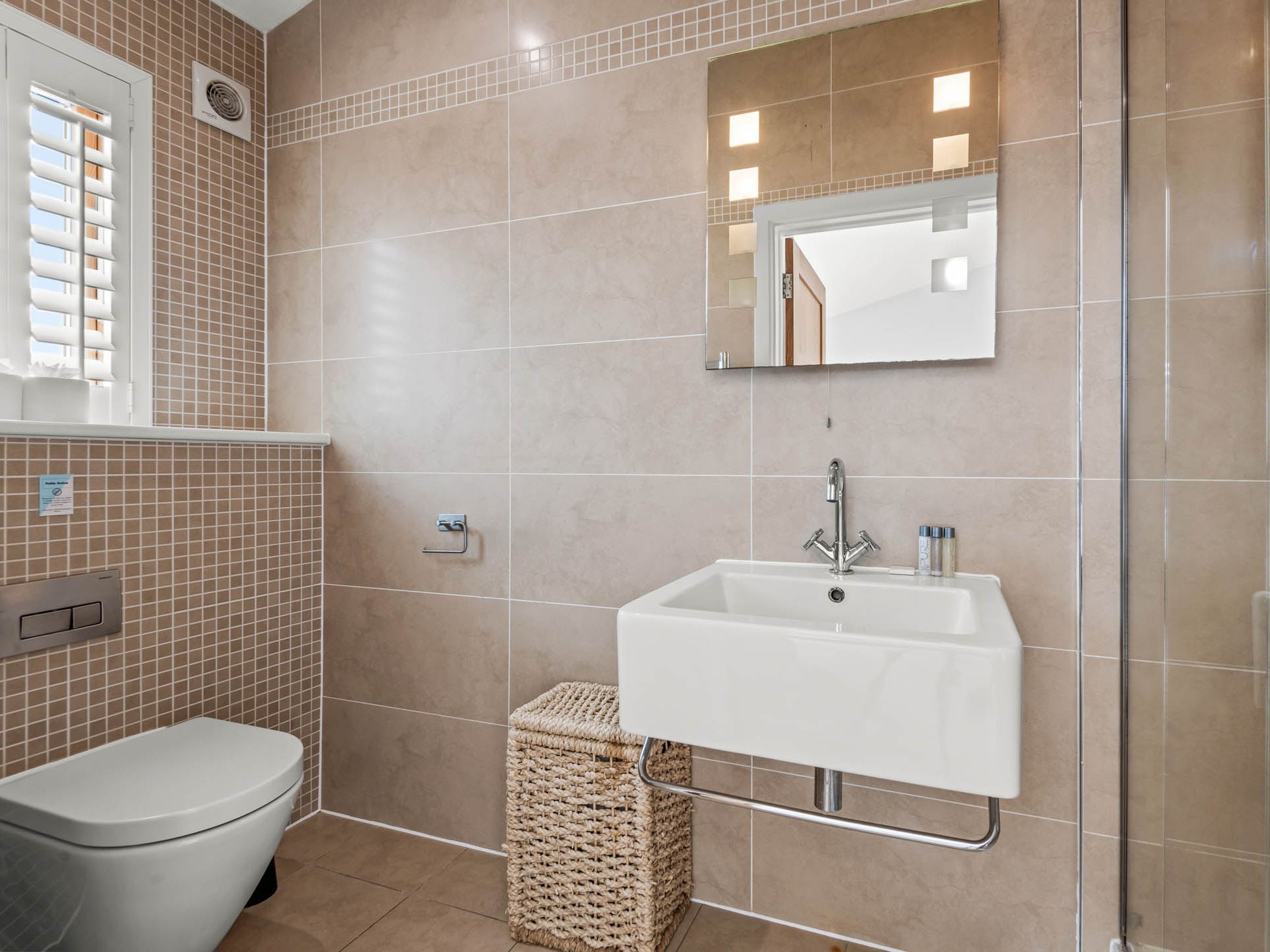 Modern tiled bathroom with wall-hung toilet, pedestal sink, mirror and glass shower enclosure