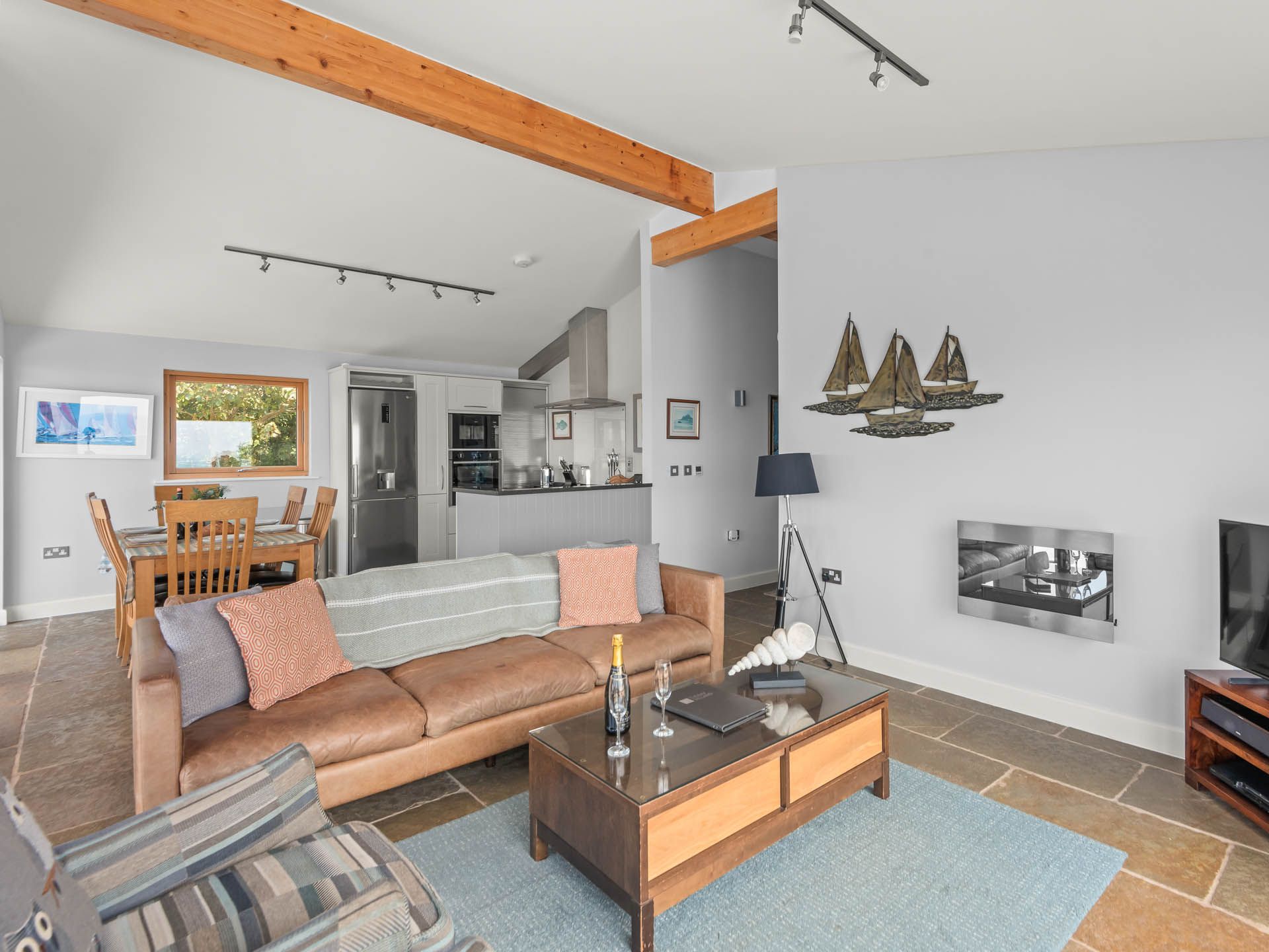 Modern open-plan living room and kitchen with exposed timber beams, leather sofa and dining table
