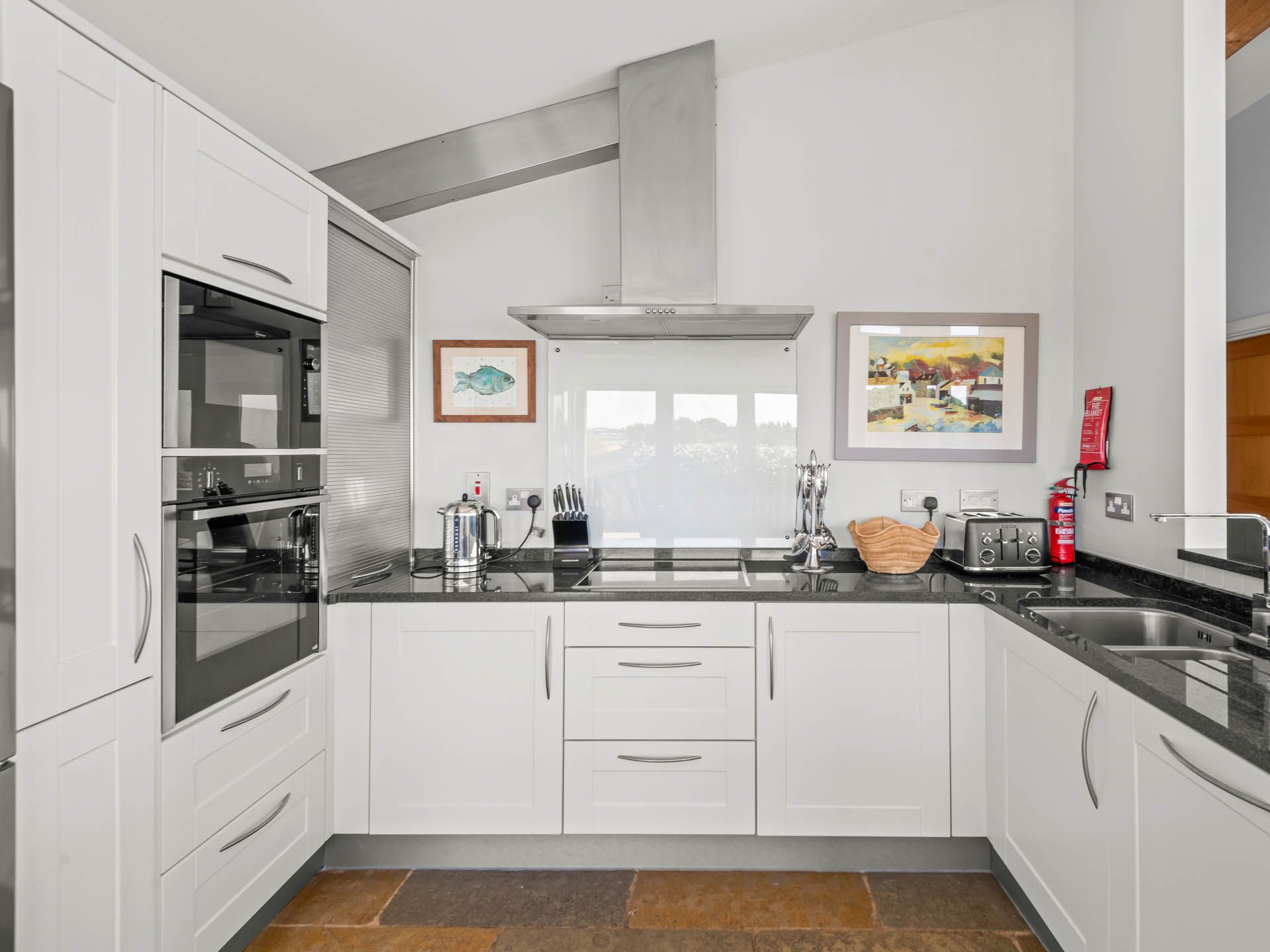 Modern white kitchen with black worktops, double oven, stainless-steel extractor hood and sink