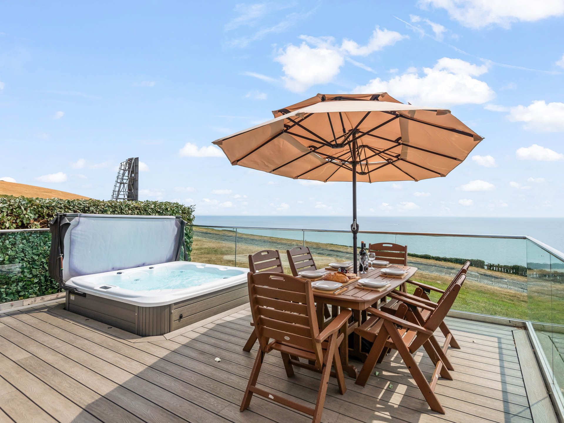 Outdoor terrace with hot tub, dining table and parasol overlooking the sea