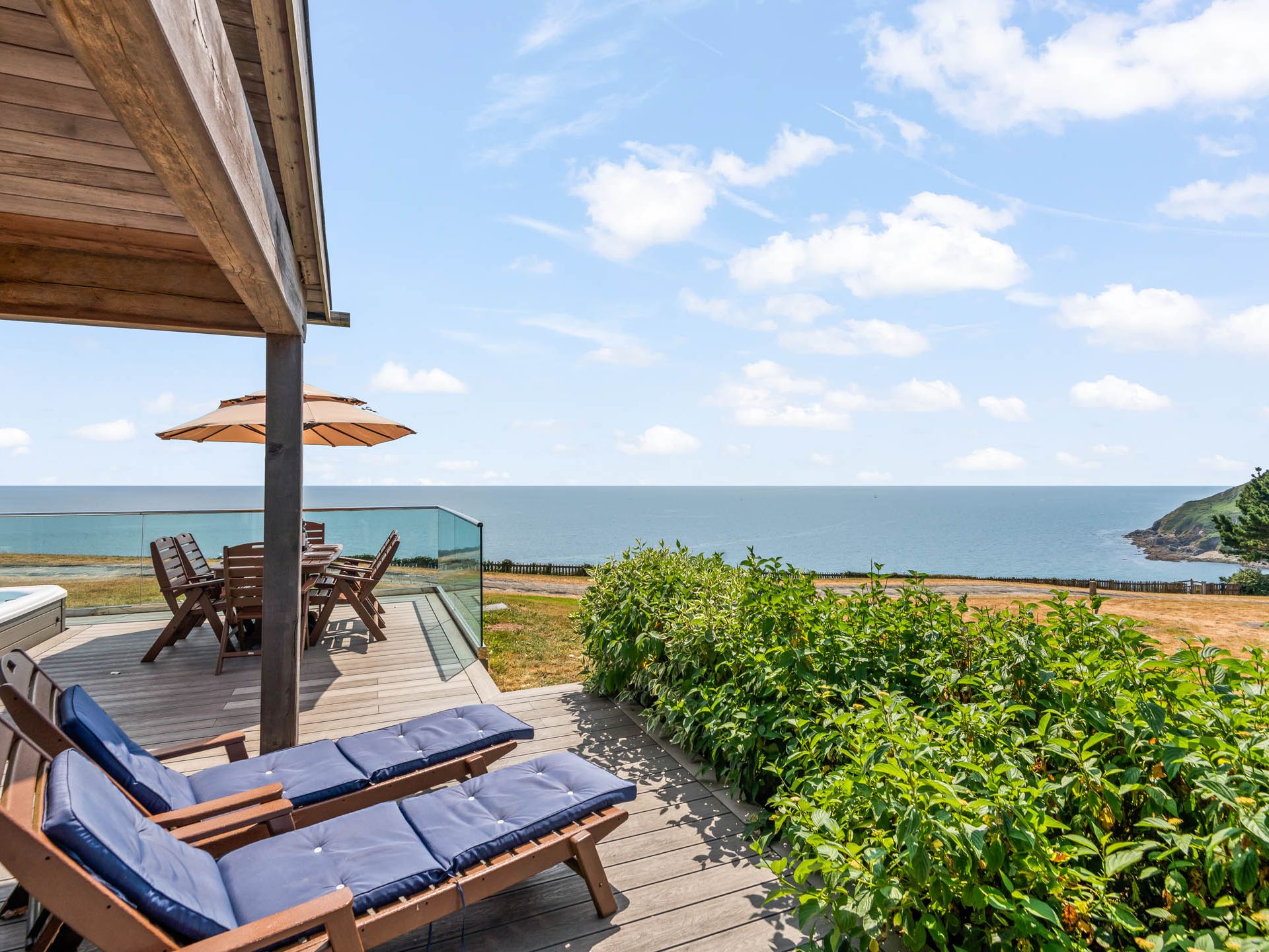 Seaside terrace with loungers, dining table and parasol overlooking the ocean