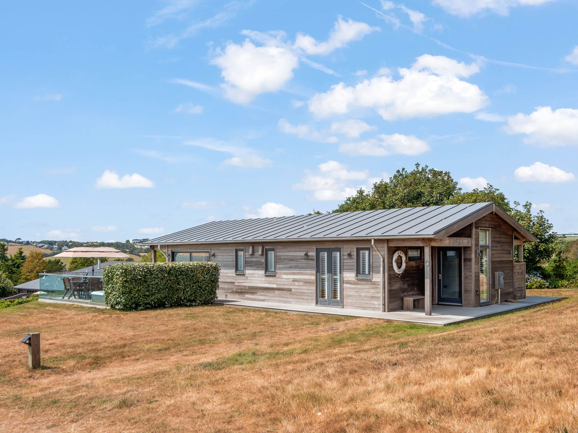 Modern wooden lodge on a grassy hillside under a blue sky with scattered clouds