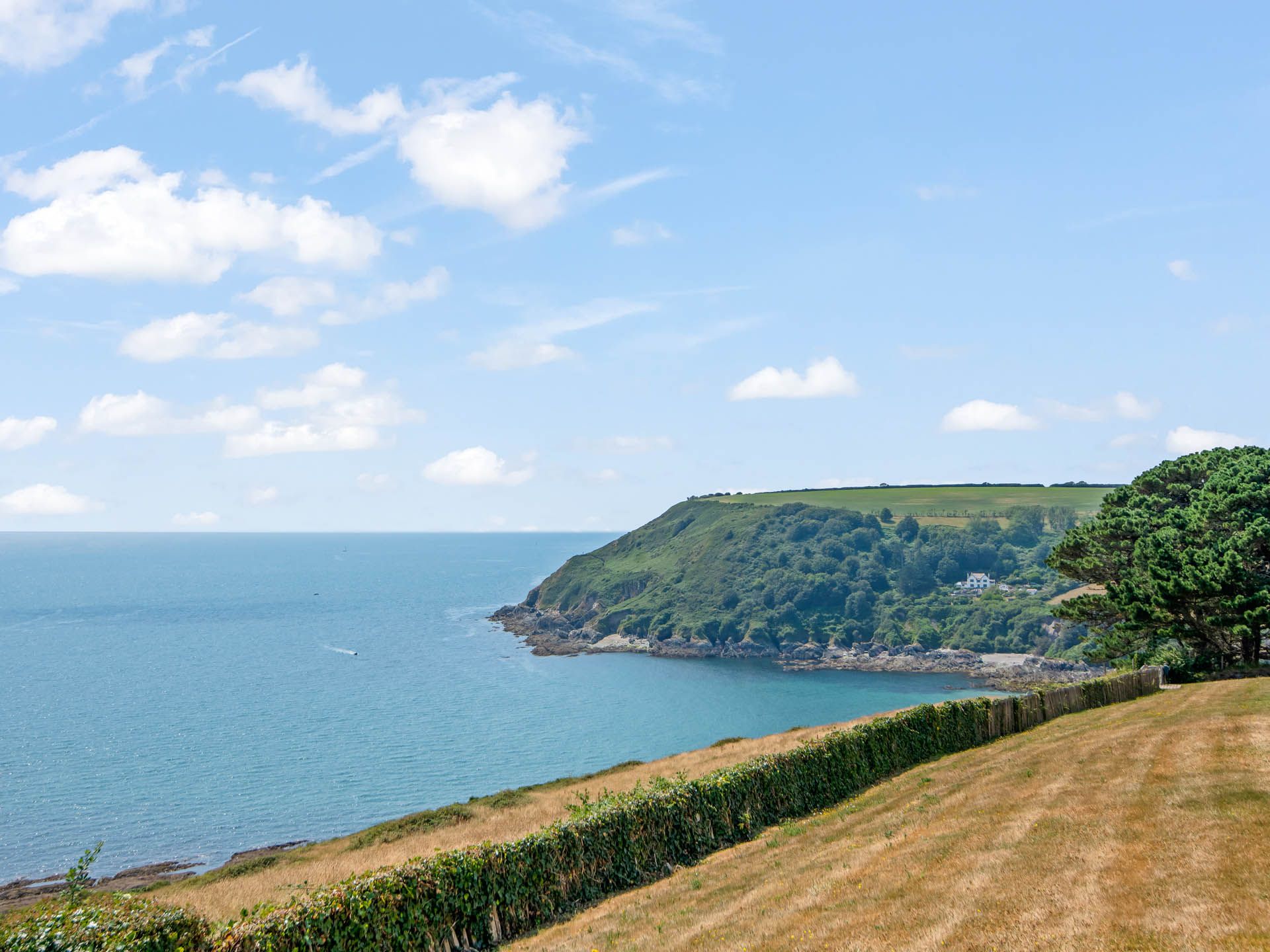 Coastal headland overlooking a calm blue sea under a bright sky with scattered clouds