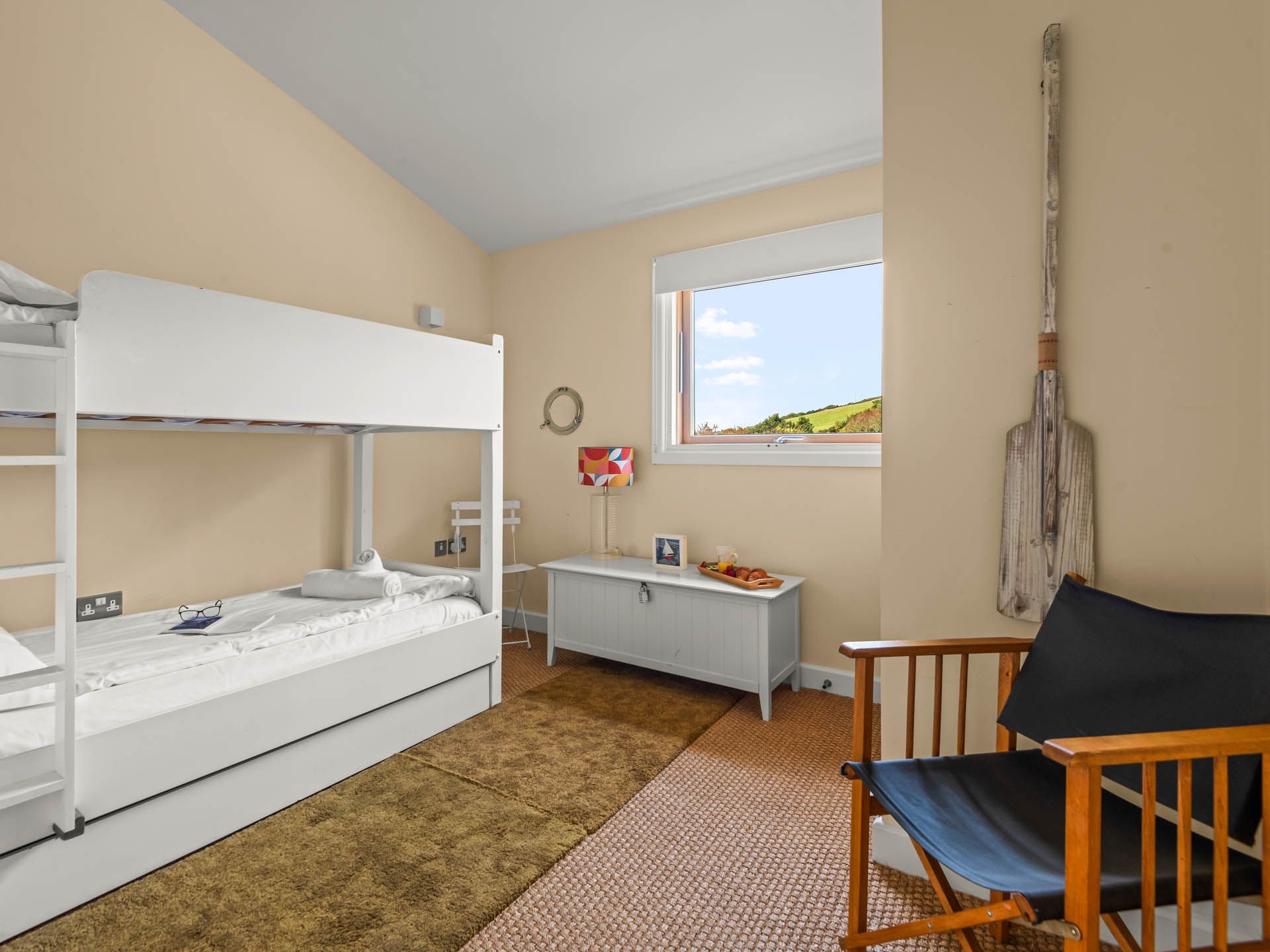 Bright bunk bedroom with white bunk beds, storage bench and countryside view through the window
