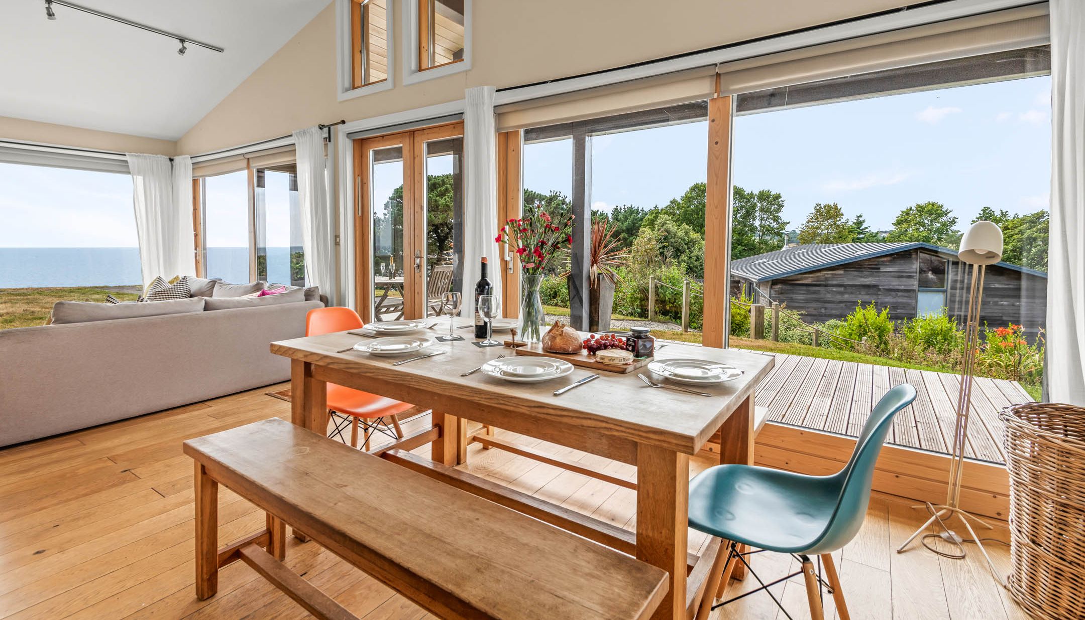 Dining table set beside floor-to-ceiling windows with sea view and garden beyond