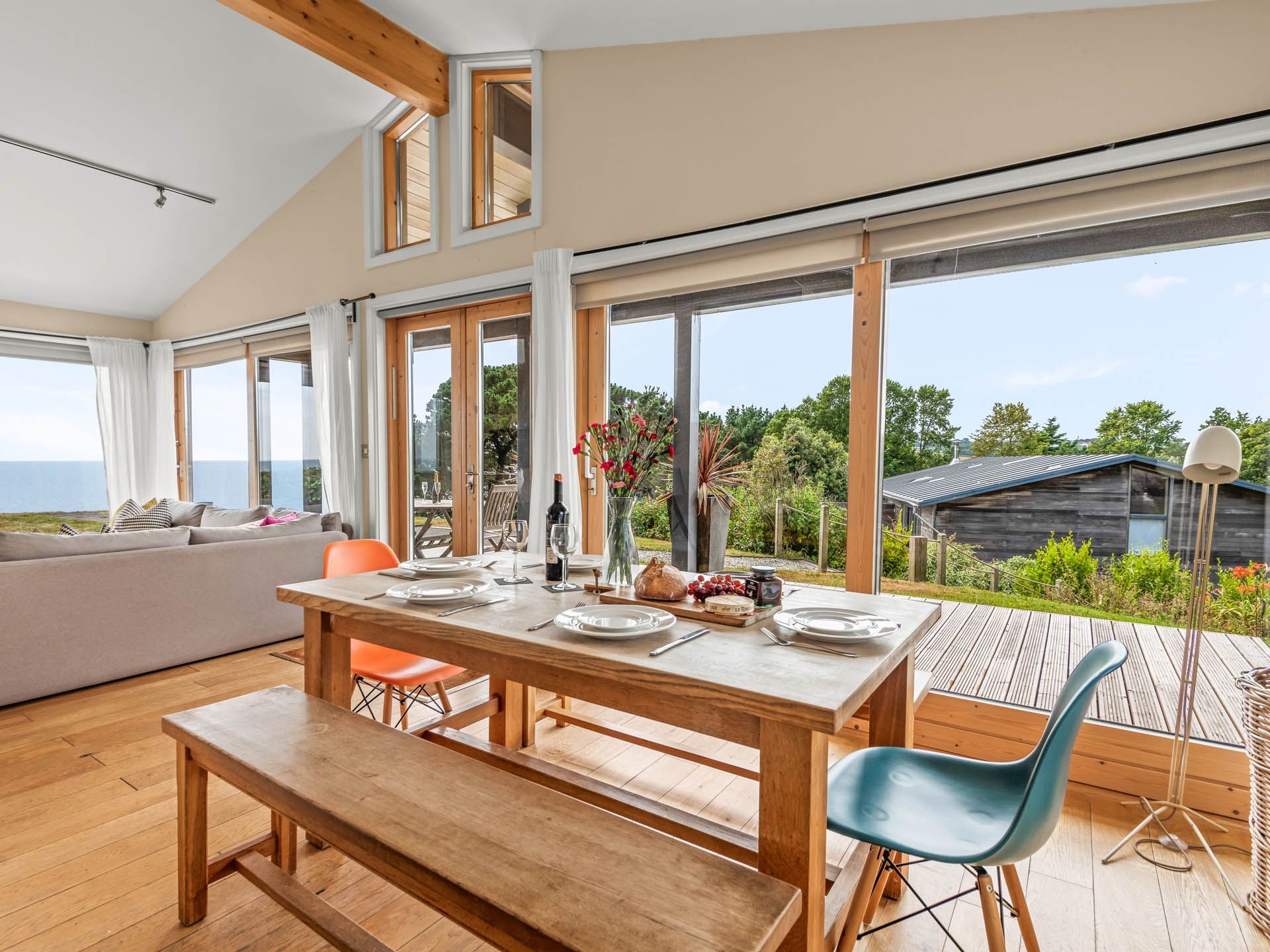 Dining table set beside floor-to-ceiling windows with sea view and garden beyond