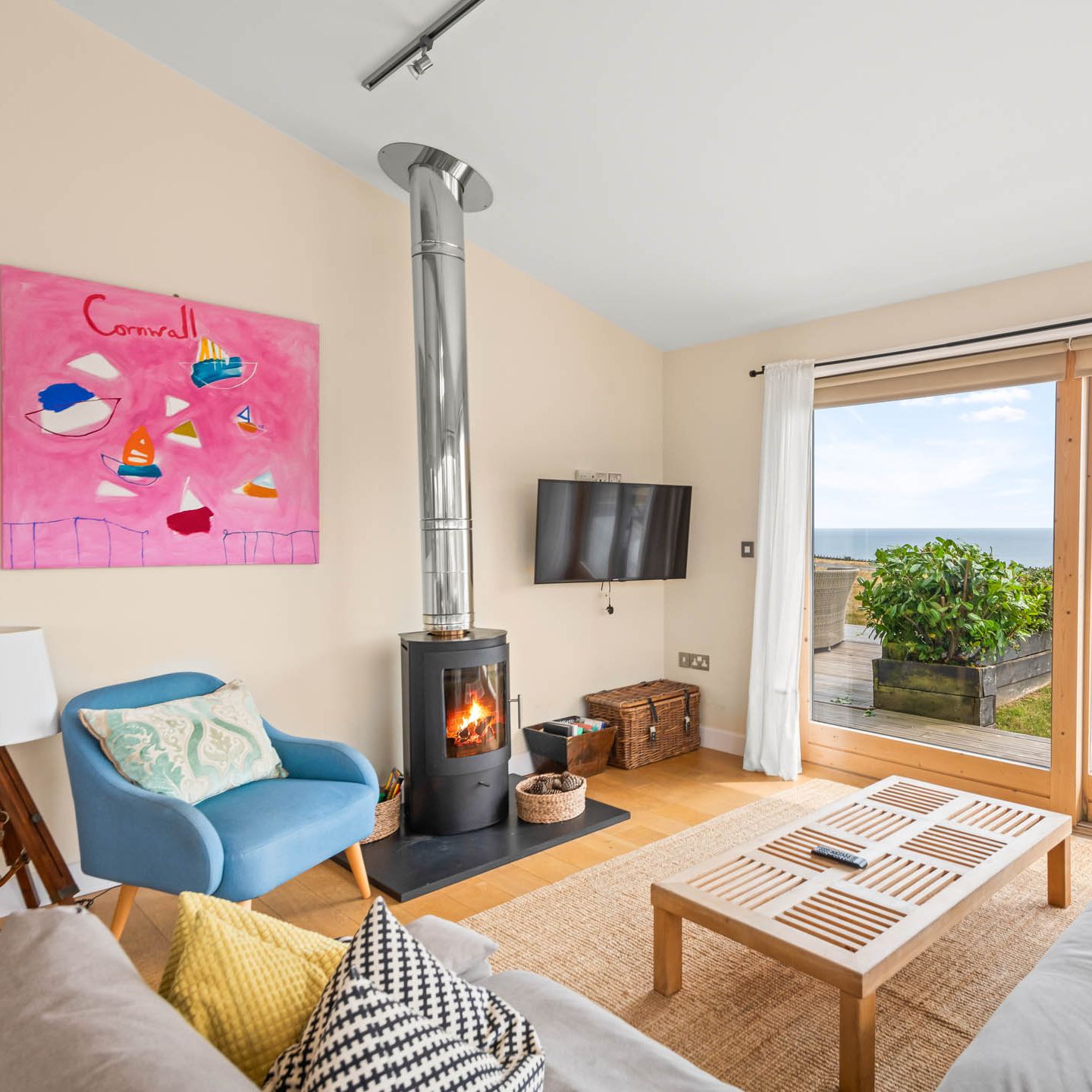 Bright coastal living room with wood-burning stove and large window overlooking the sea