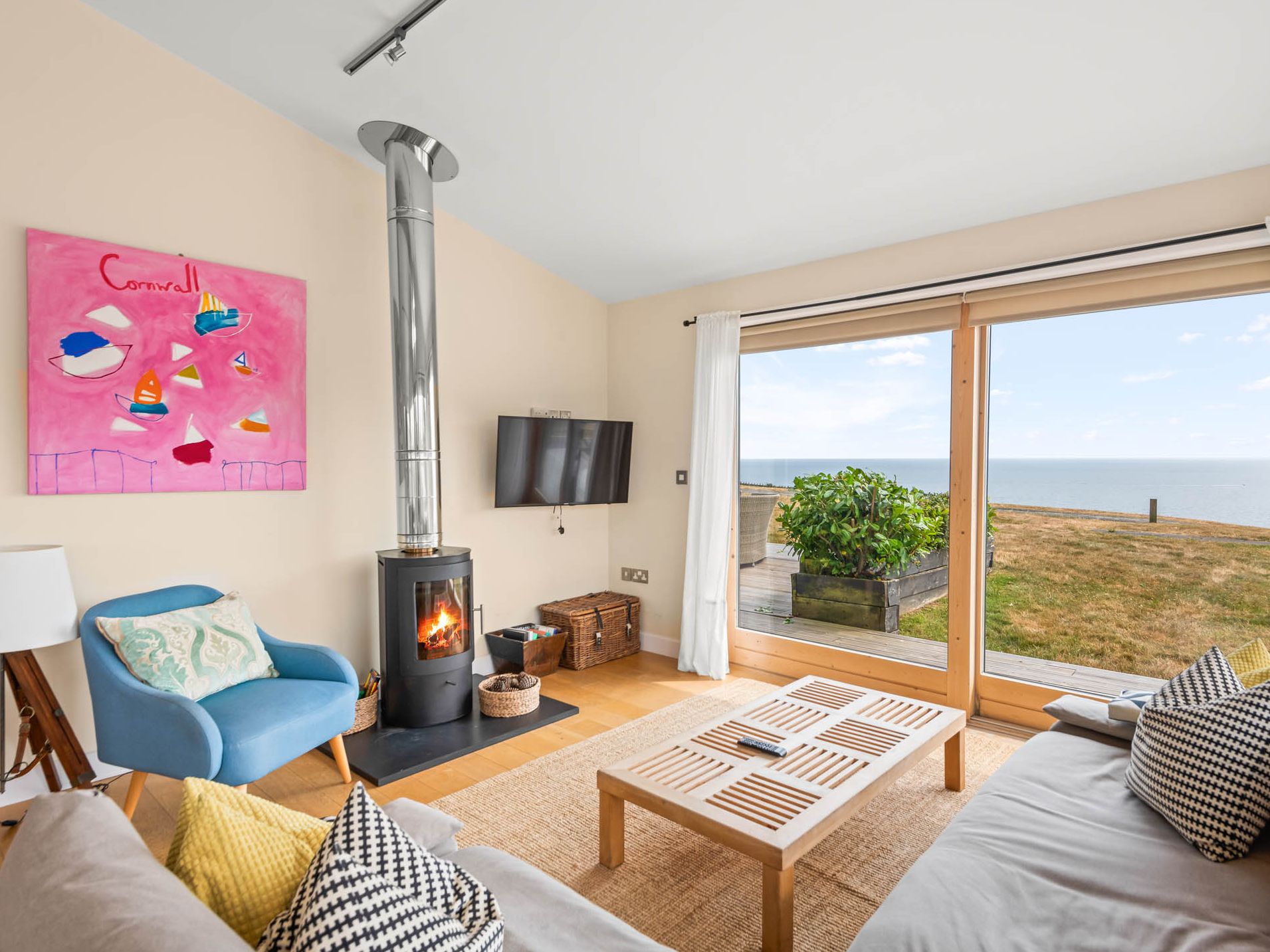 Bright coastal living room with wood-burning stove and large window overlooking the sea