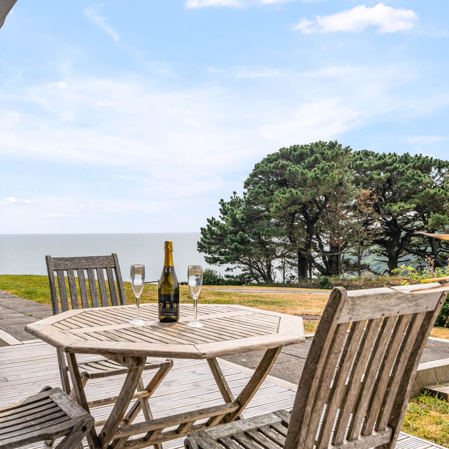 Wooden patio table with a bottle of sparkling wine and two flutes overlooking the sea
