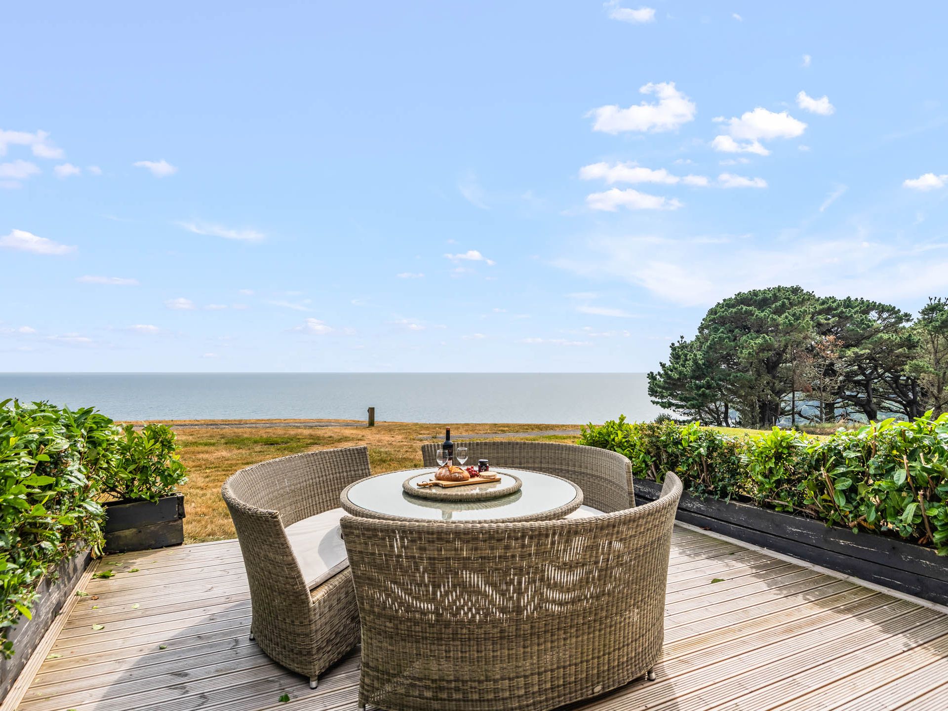 Wicker patio dining set on a wooden deck overlooking the sea under a blue sky