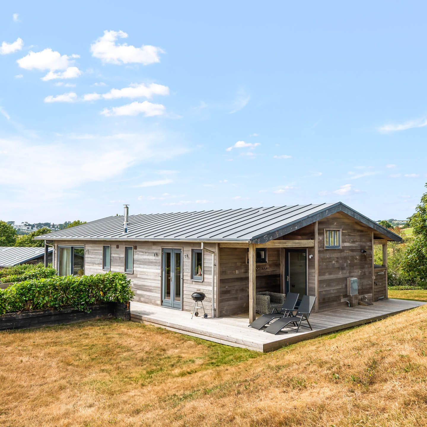Modern wooden lodge with deck chairs on a hillside under a blue sky