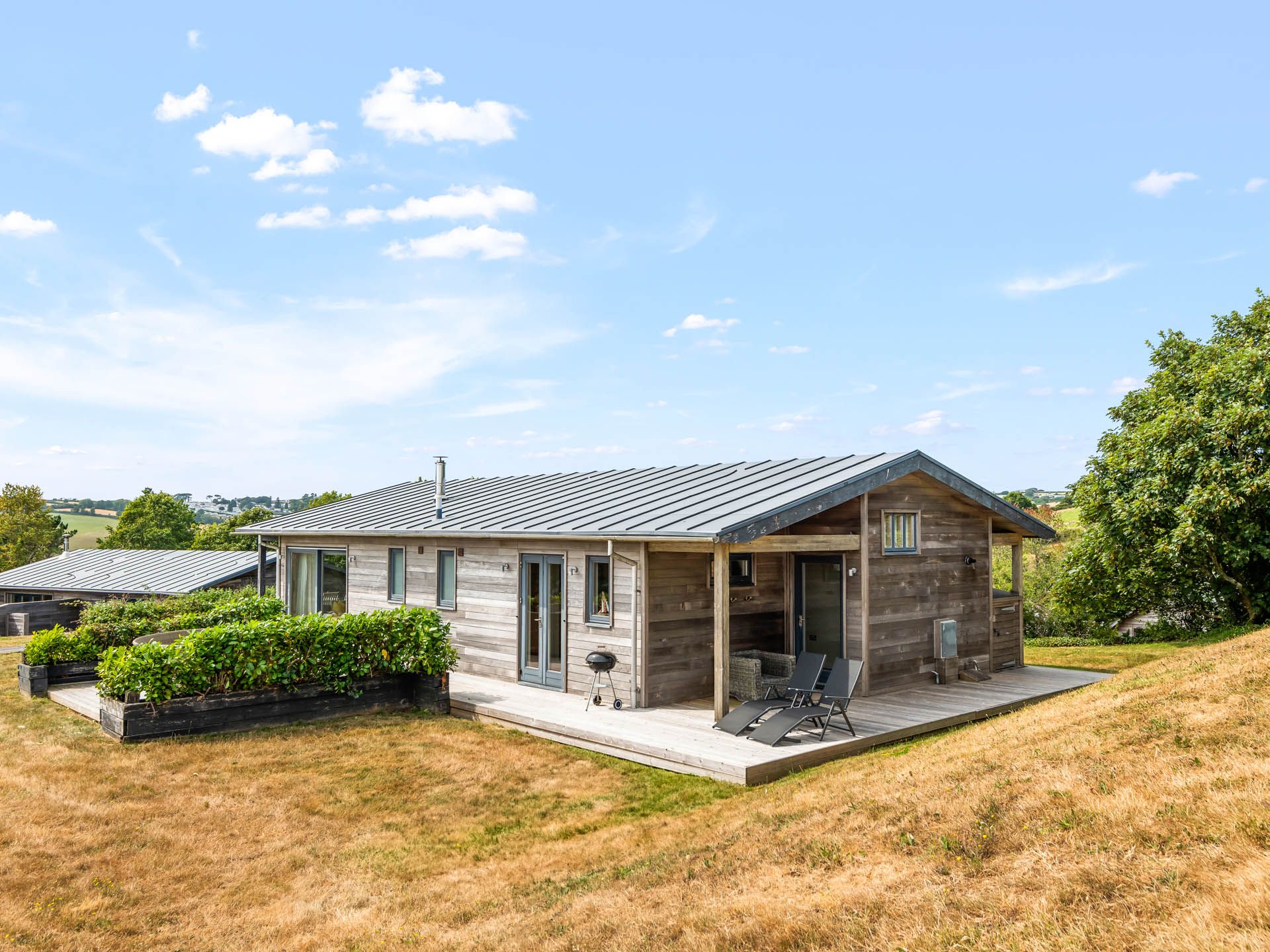 Modern wooden lodge with deck chairs on a hillside under a blue sky