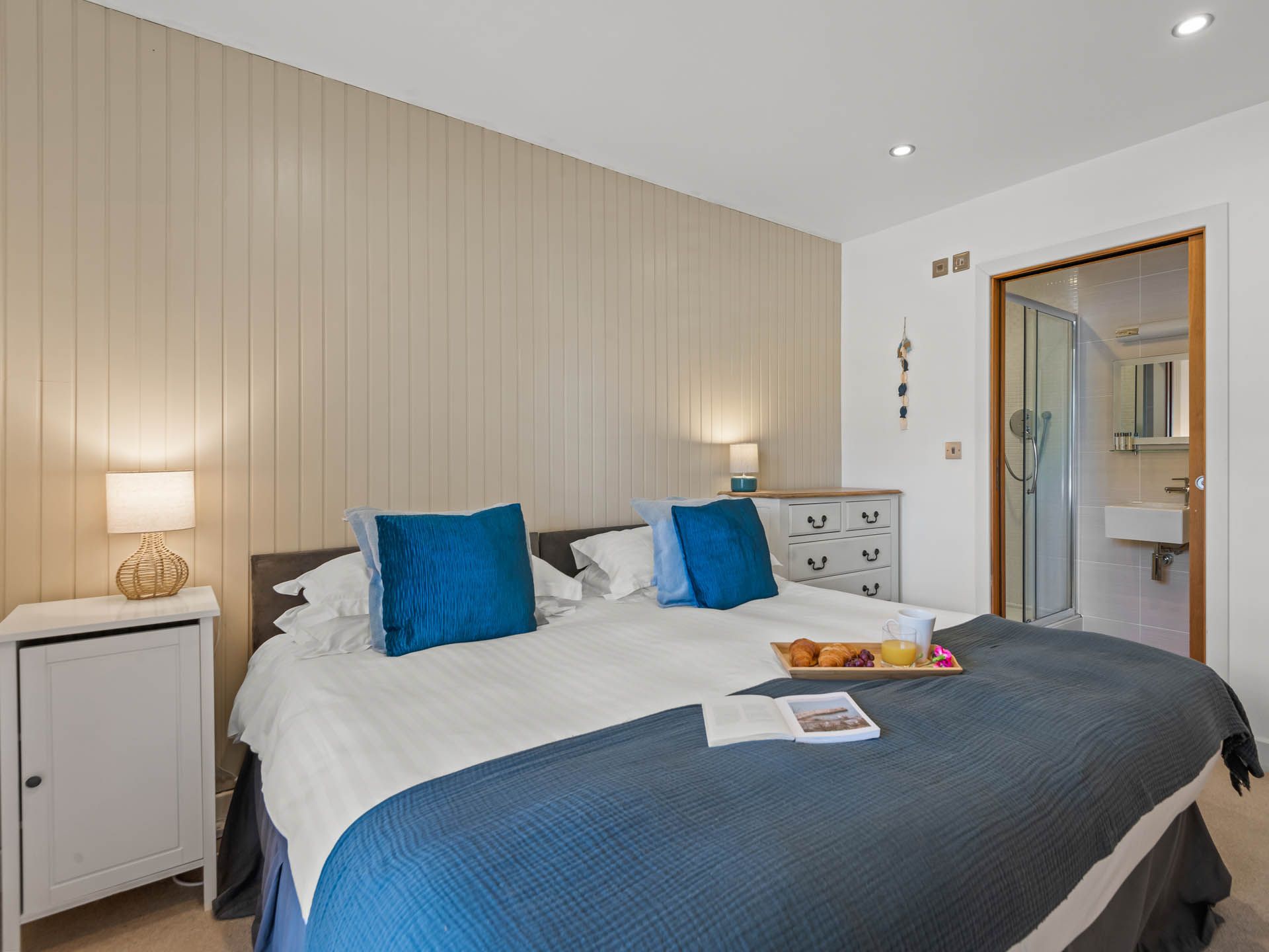 Bright double bedroom with blue cushions, bedside lamps and en-suite bathroom