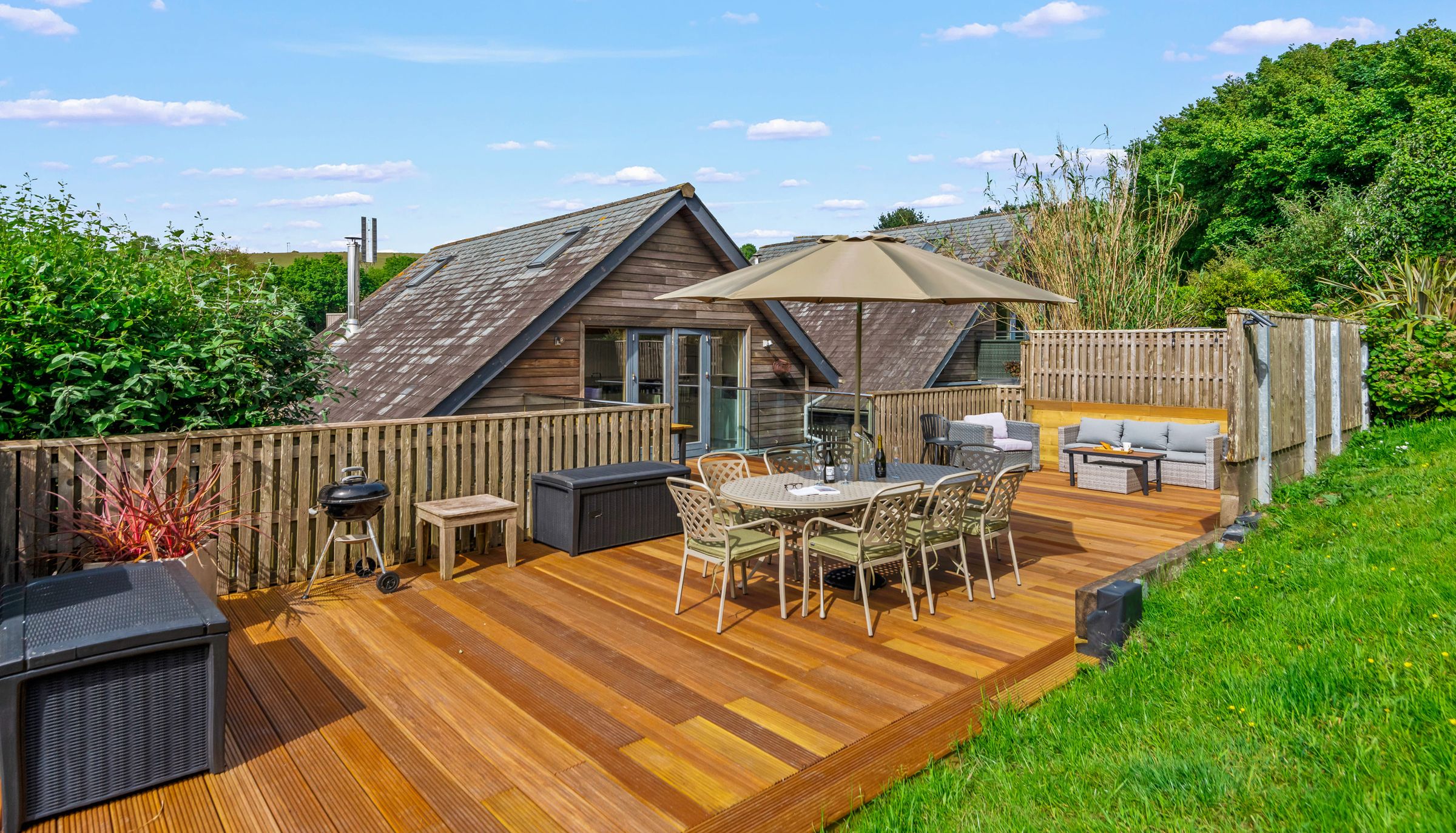 Wooden lodge with spacious deck, outdoor dining set and parasol under a blue sky