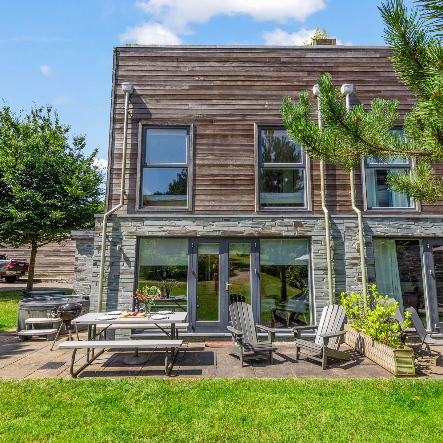 Modern timber-clad building with stone base and patio seating on a sunny day