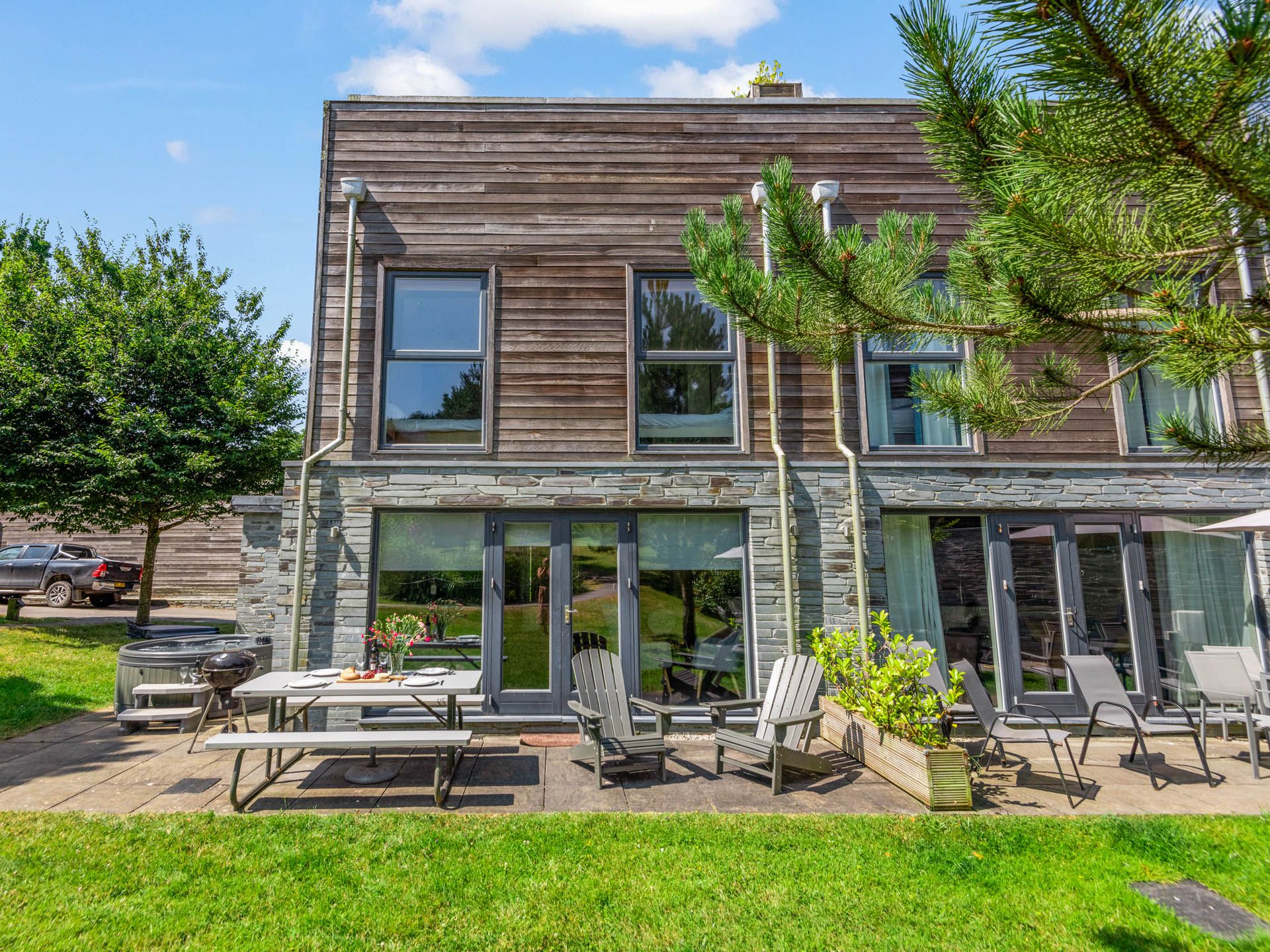 Modern timber-clad building with stone base and patio seating on a sunny day