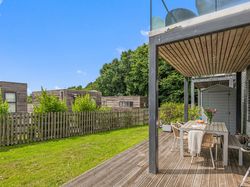 Modern patio with outdoor dining set in a fenced backyard, adjacent to wooden houses and greenery