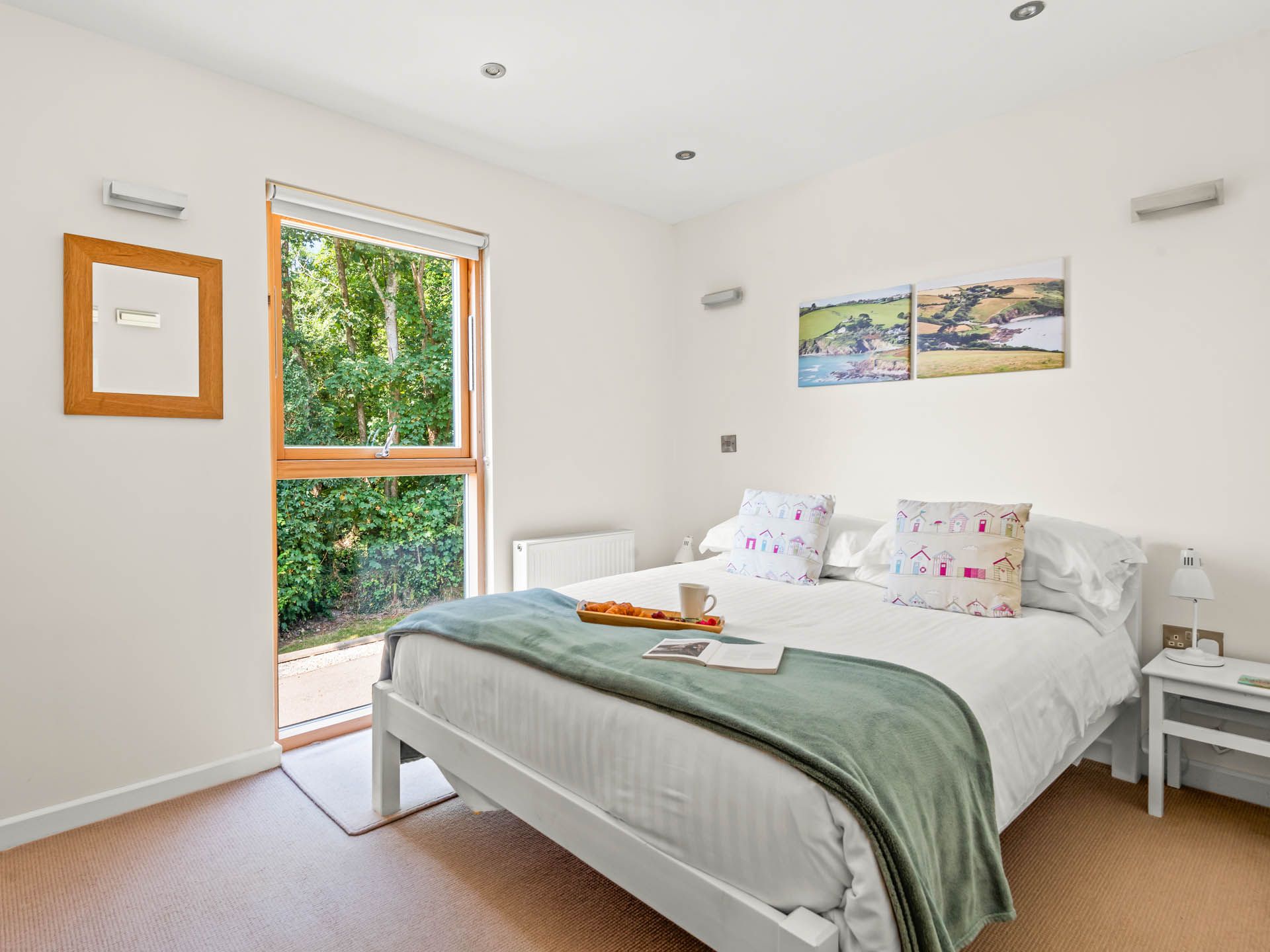 Bright bedroom with double bed, green throw and large window overlooking trees