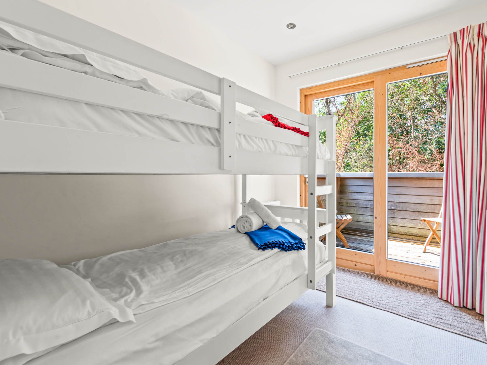 Bright bedroom with white bunk beds beside glass doors opening onto a small balcony