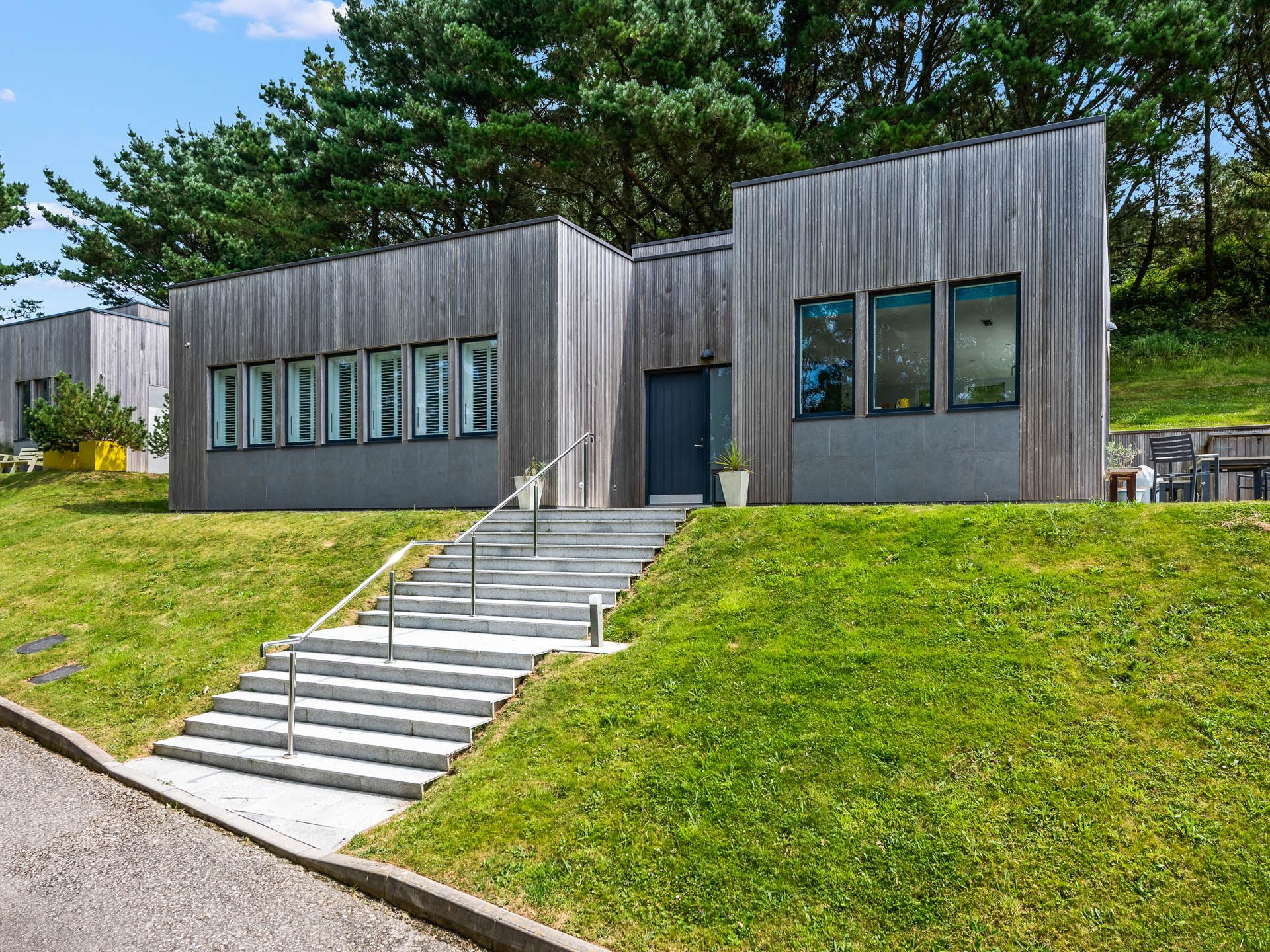 Modern timber-clad building on a grassy slope with steps leading to the entrance