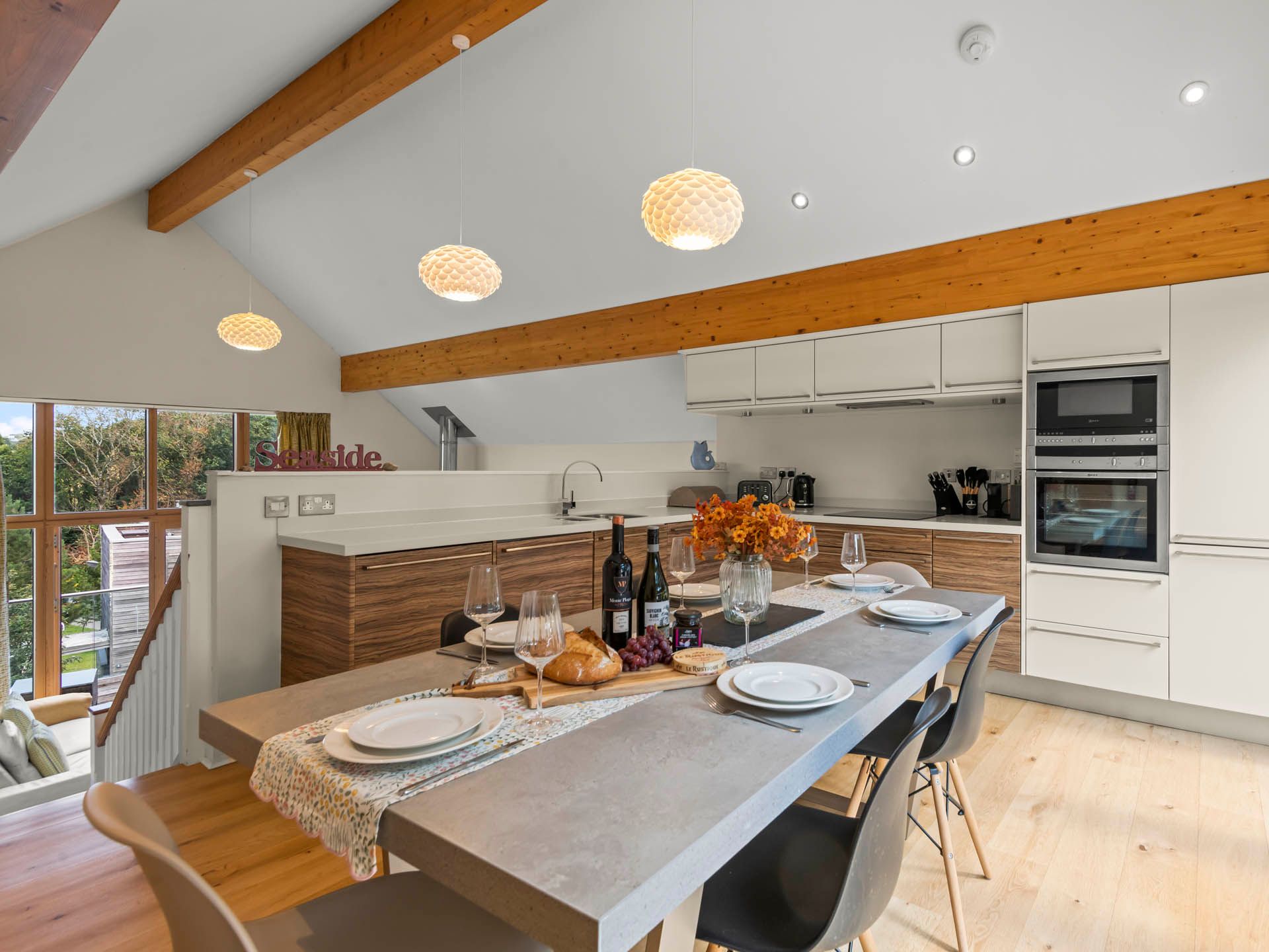 Modern open-plan kitchen and dining area with timber beams, pendant lights and a laid table