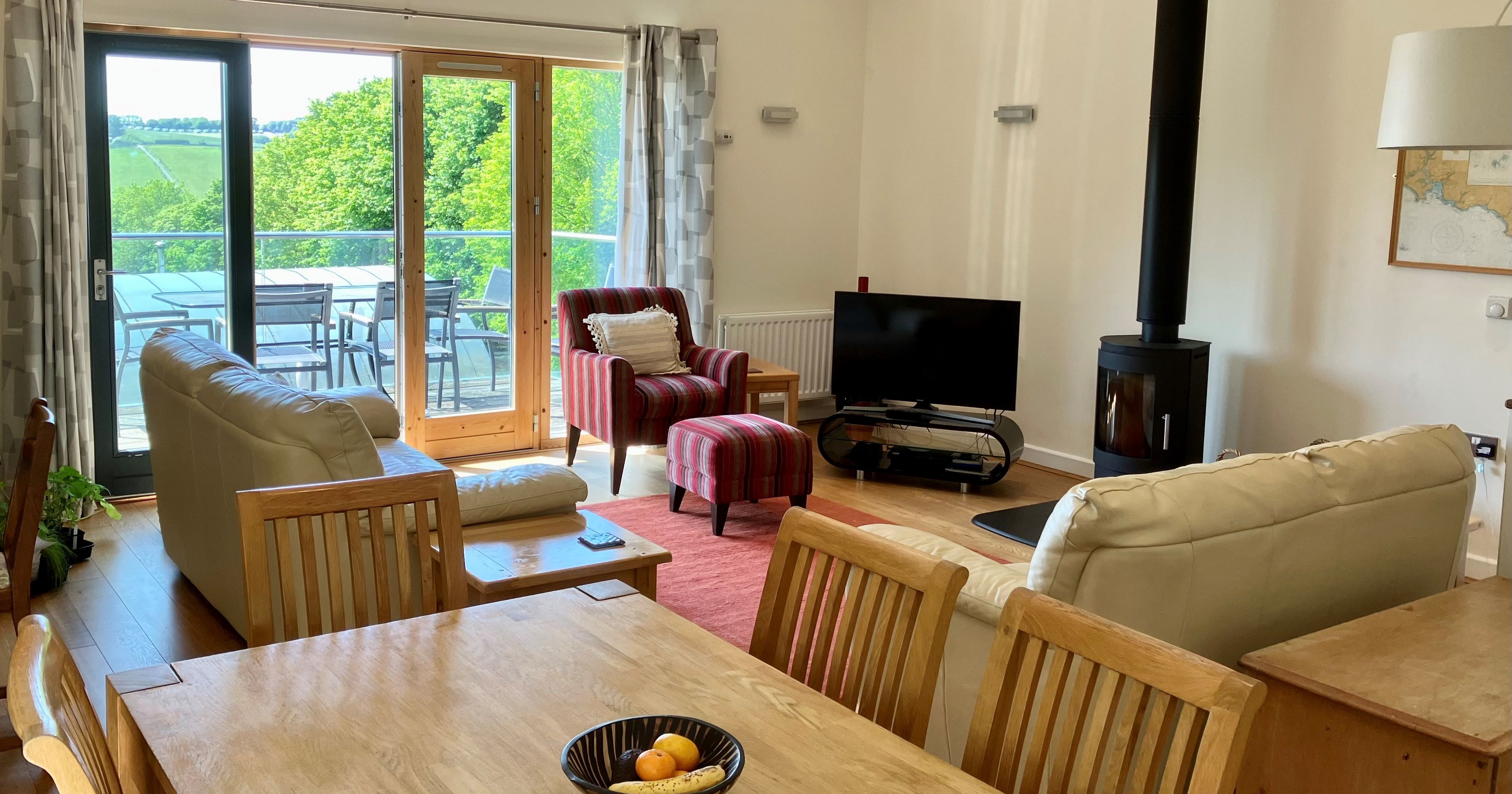 Modern living and dining room with large glass doors opening to a balcony with outdoor seating and scenic views