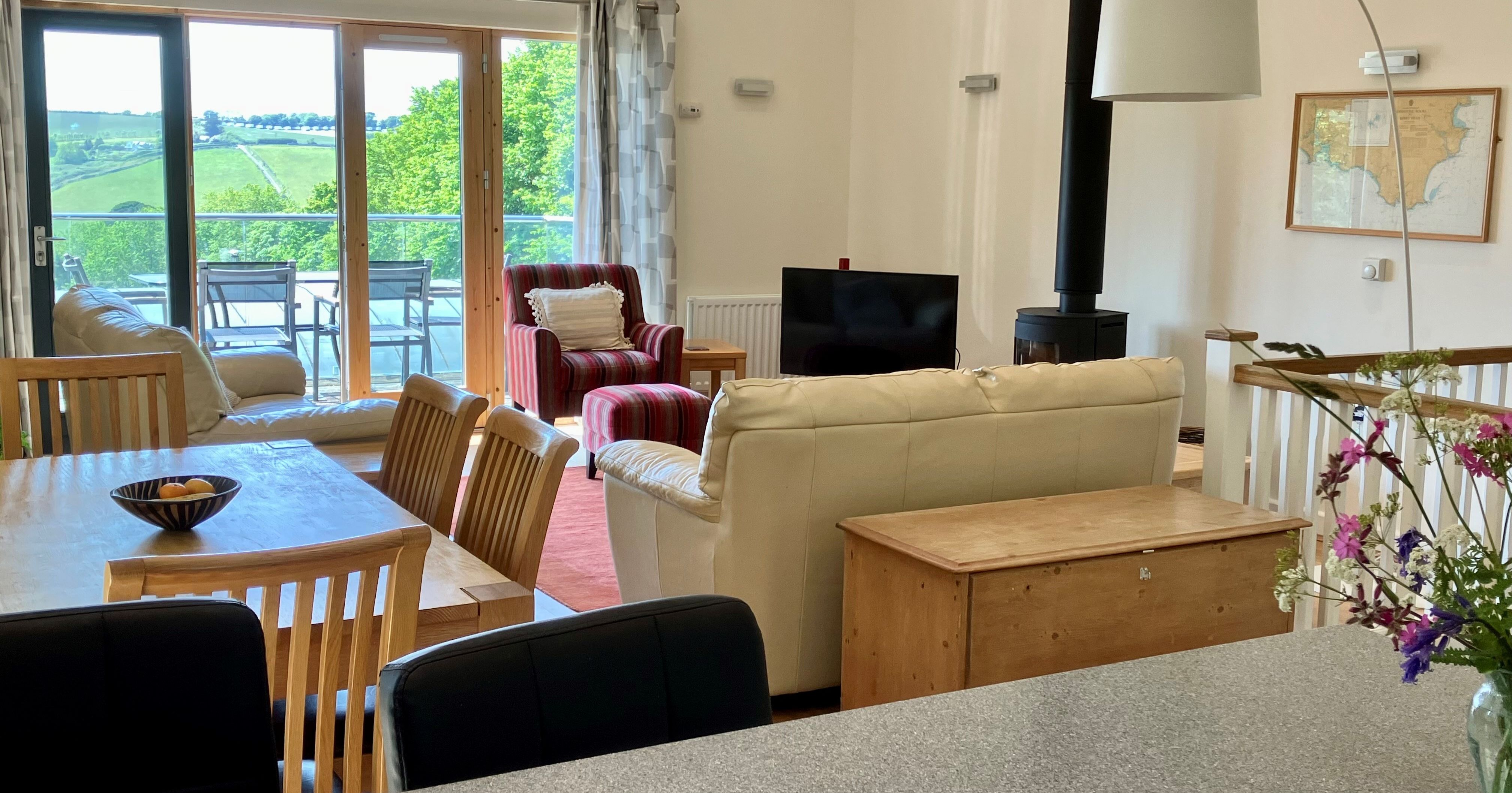 Bright and spacious living and dining area with large windows, comfortable seating, and a view of green hills outside.