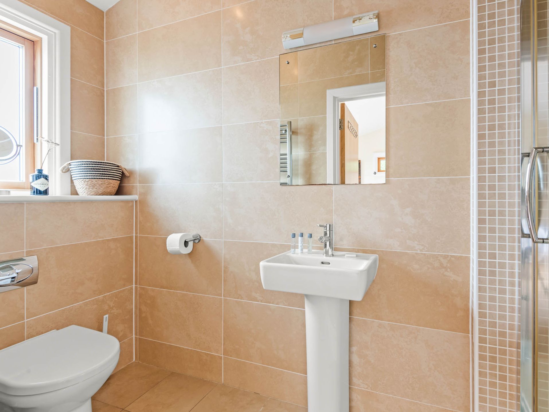 Modern tiled bathroom with pedestal sink, wall mirror and glass shower enclosure
