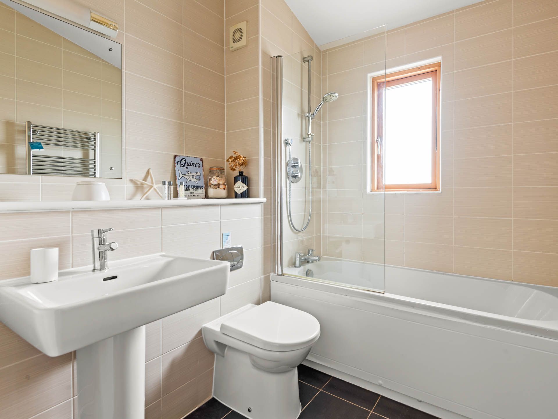 Bright modern bathroom with bath and overhead shower, basin, toilet and window