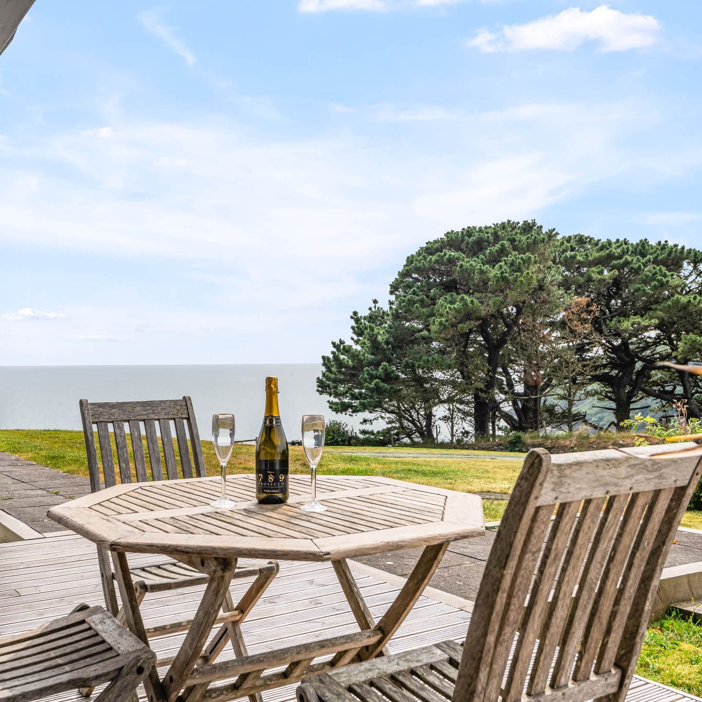 Wooden patio table with a bottle of sparkling wine and two glasses overlooking the sea