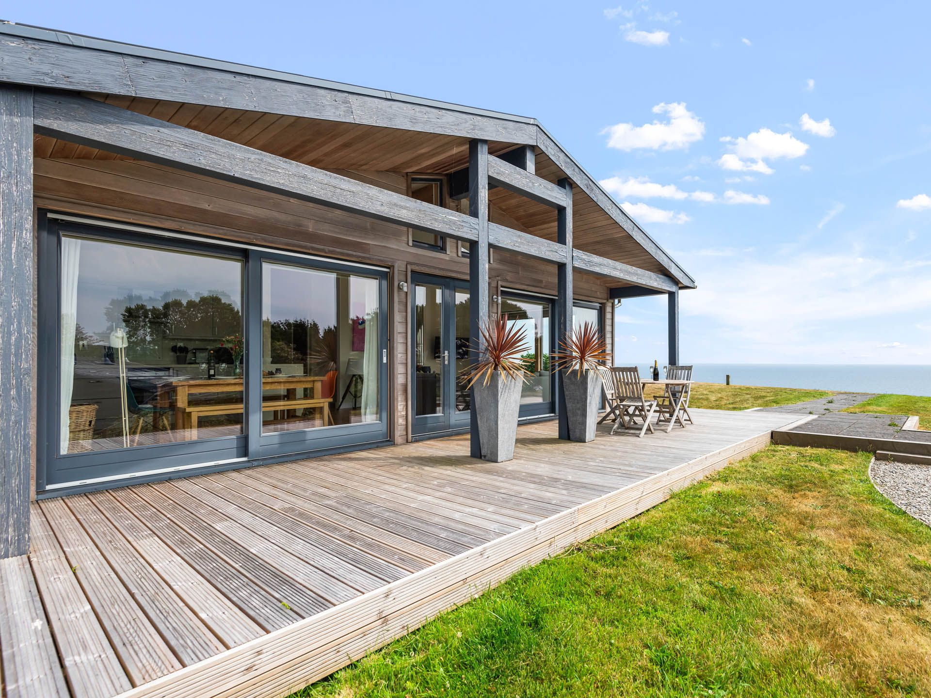 Modern timber-clad house with large glass doors and a wooden deck overlooking the sea