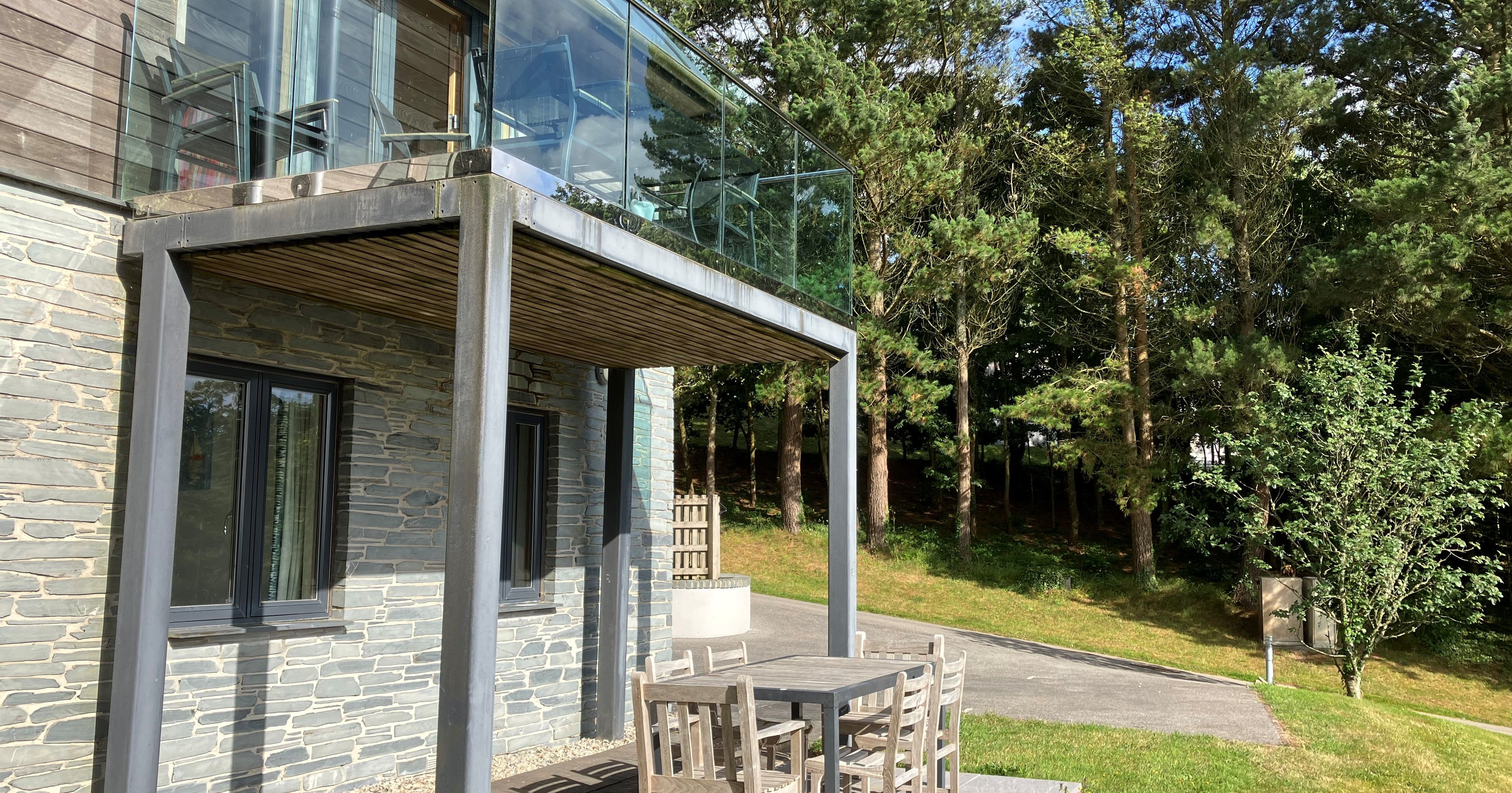 Modern house with glass balcony and outdoor dining set surrounded by grass and trees