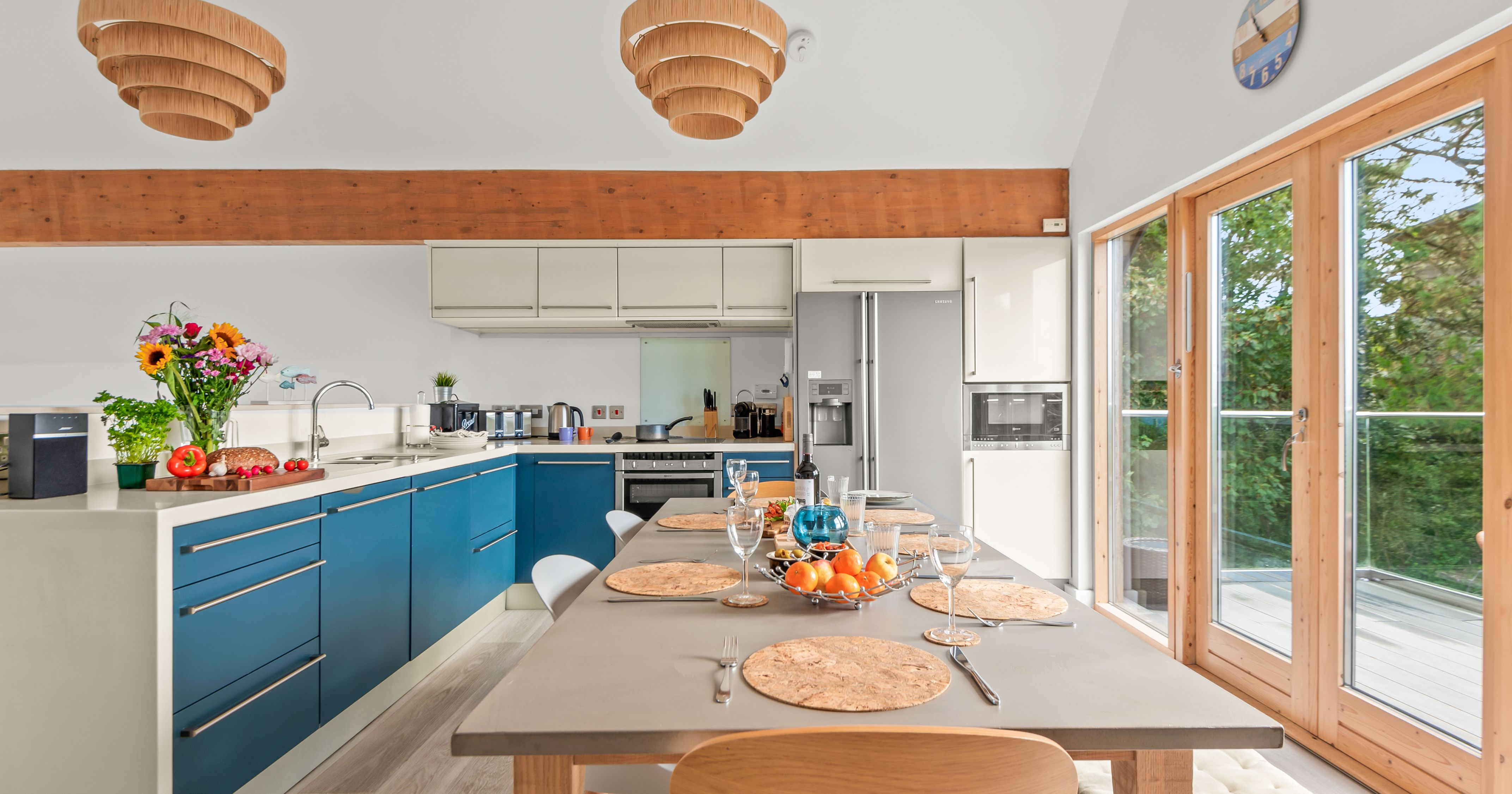 Modern kitchen and dining area with blue cabinets, wooden accents, and large glass doors overlooking greenery.