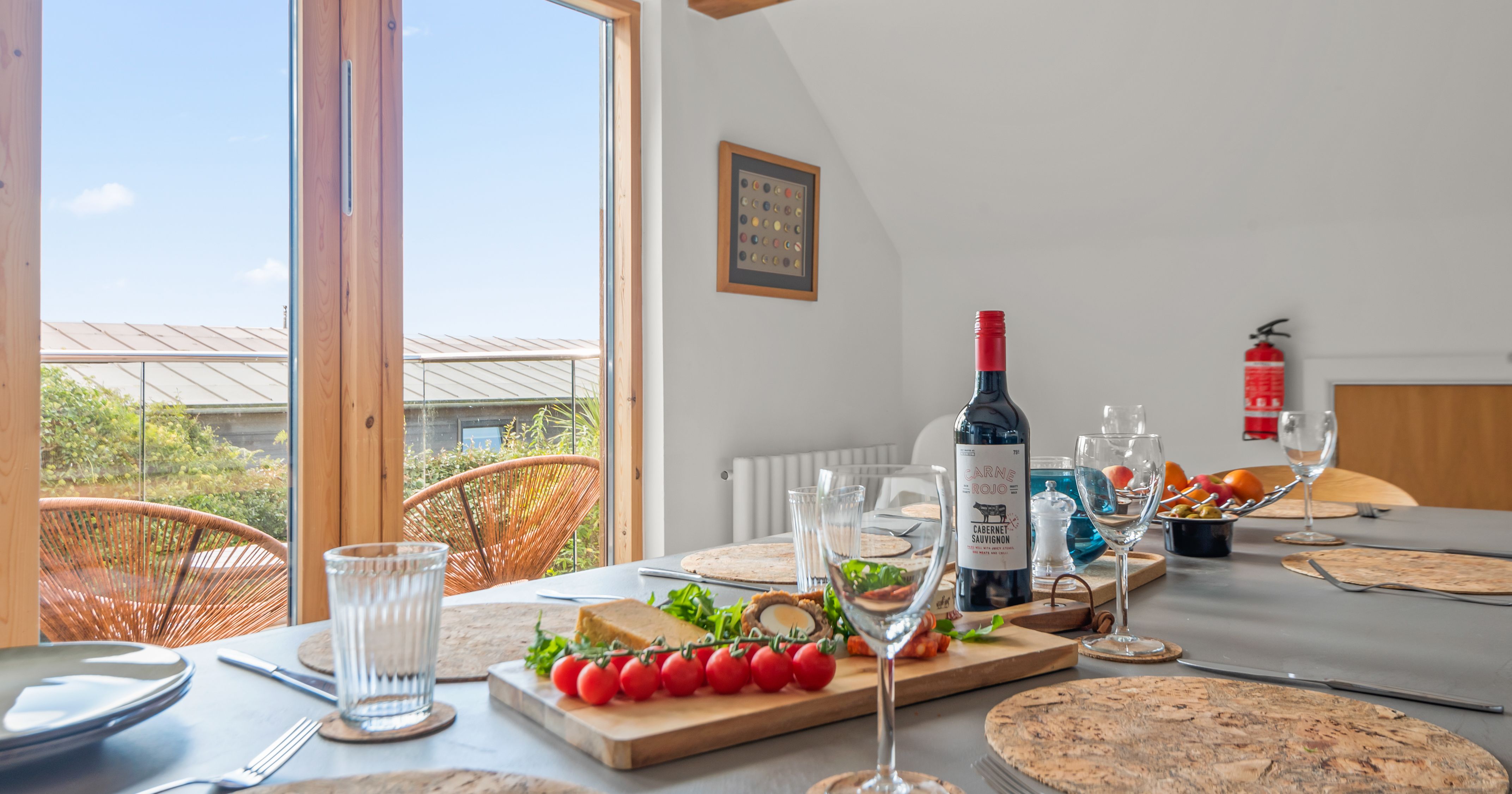Dining table set with wine, glasses, and food near glass doors to outdoor seating