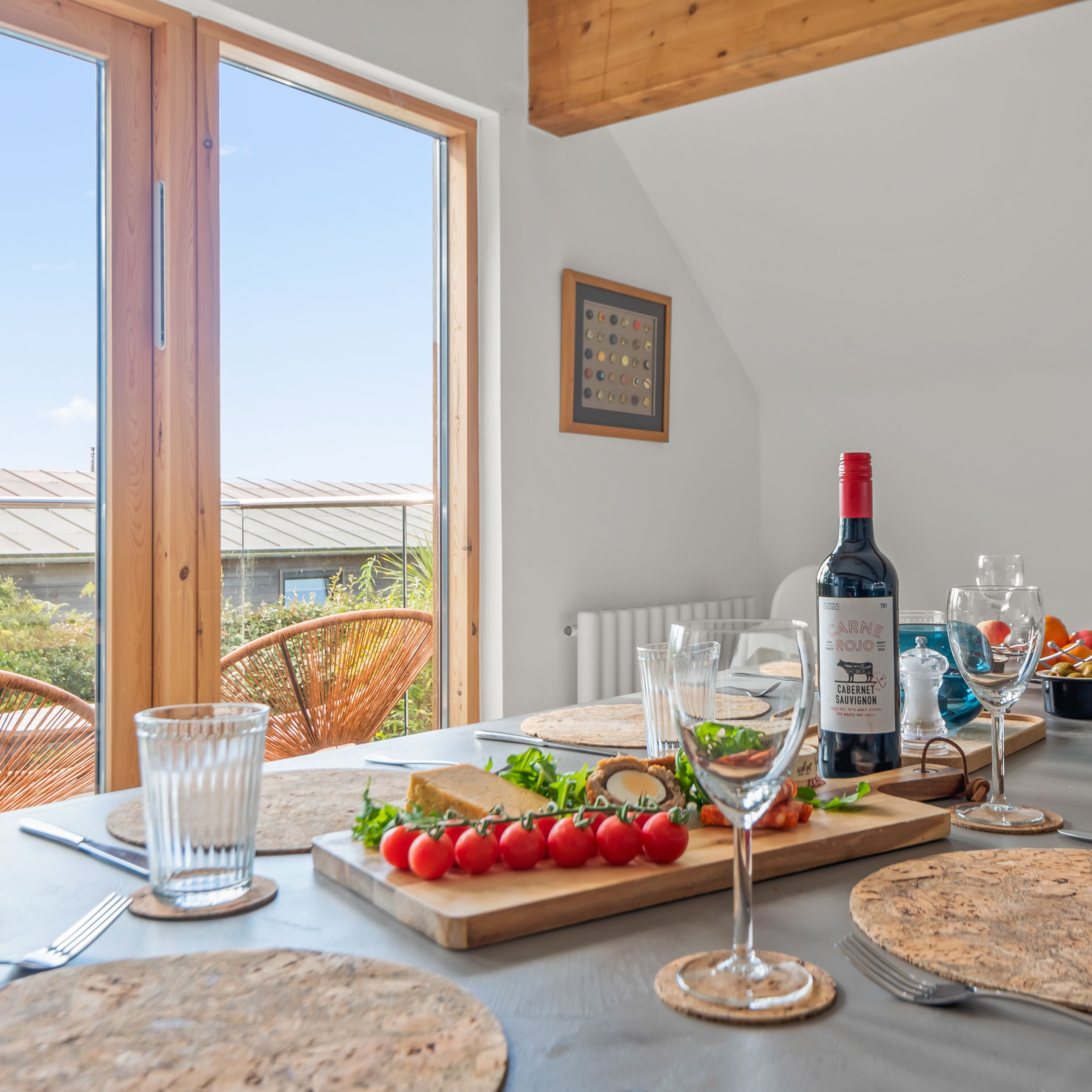 Dining table set with wine, glasses, and food near glass doors to outdoor seating