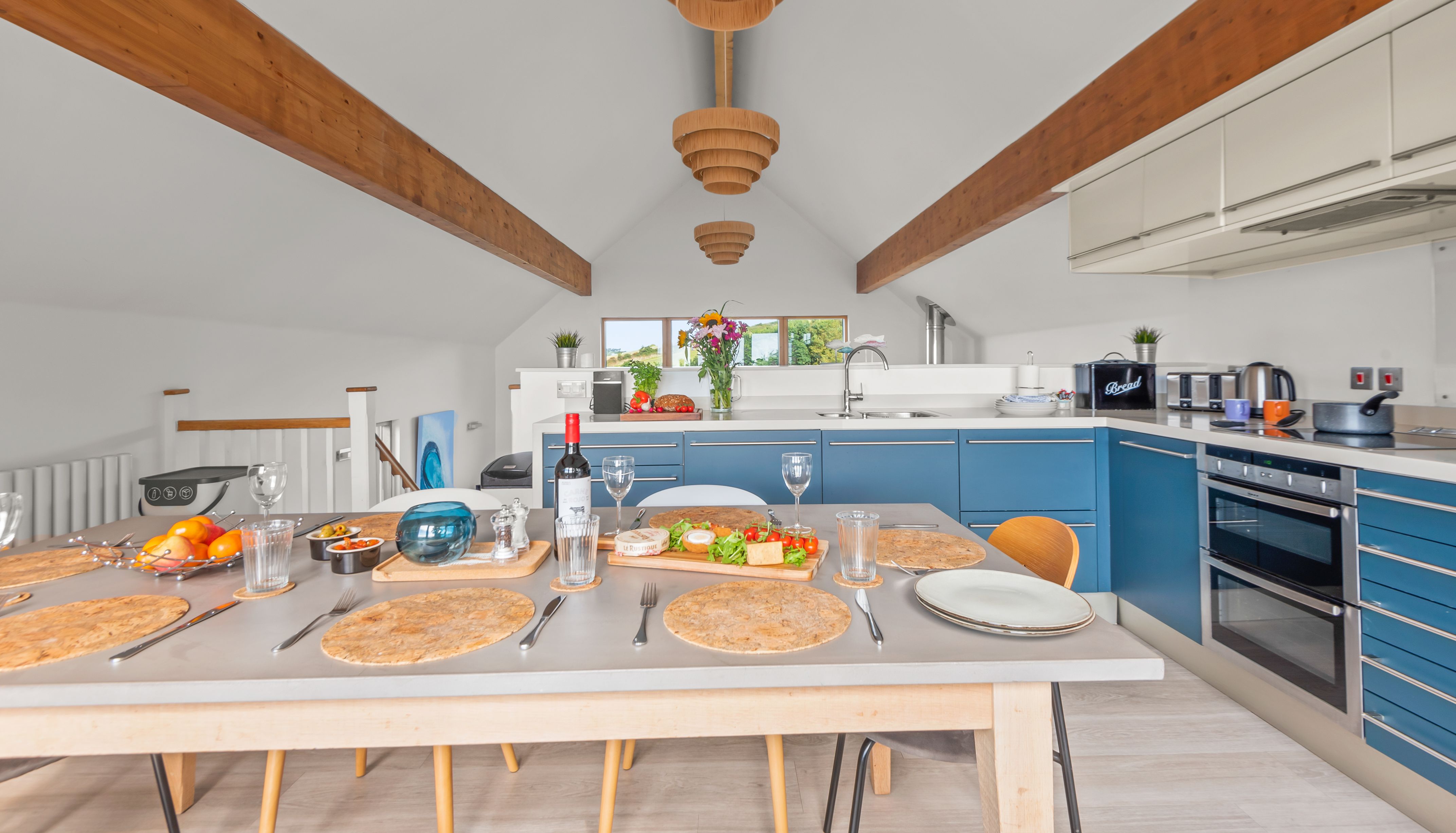 Modern kitchen and dining area with blue cabinets, set dining table, and wooden beams on the ceiling