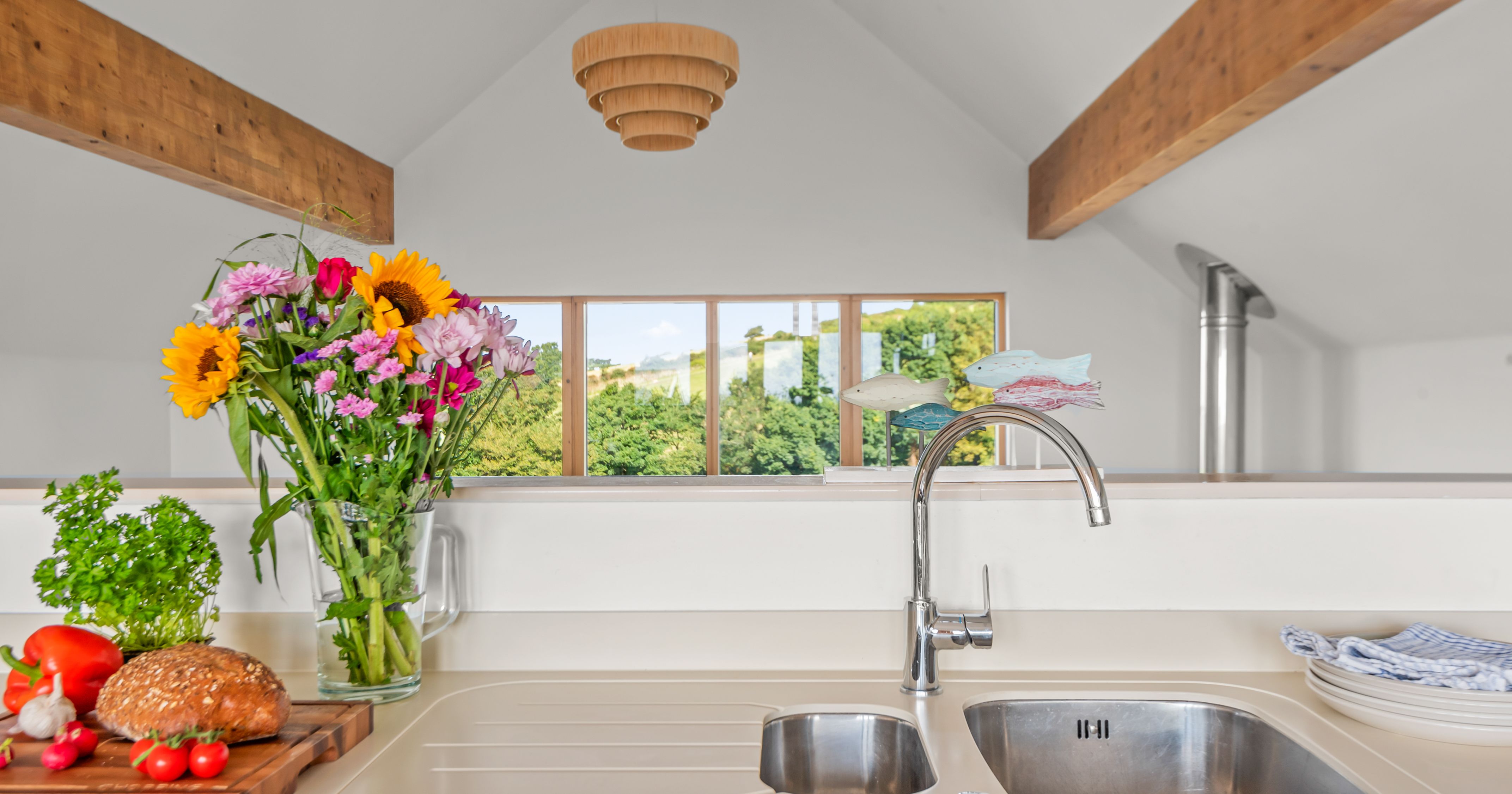 Modern kitchen countertop with a sink, bouquet of flowers, fresh vegetables, and a loaf of bread