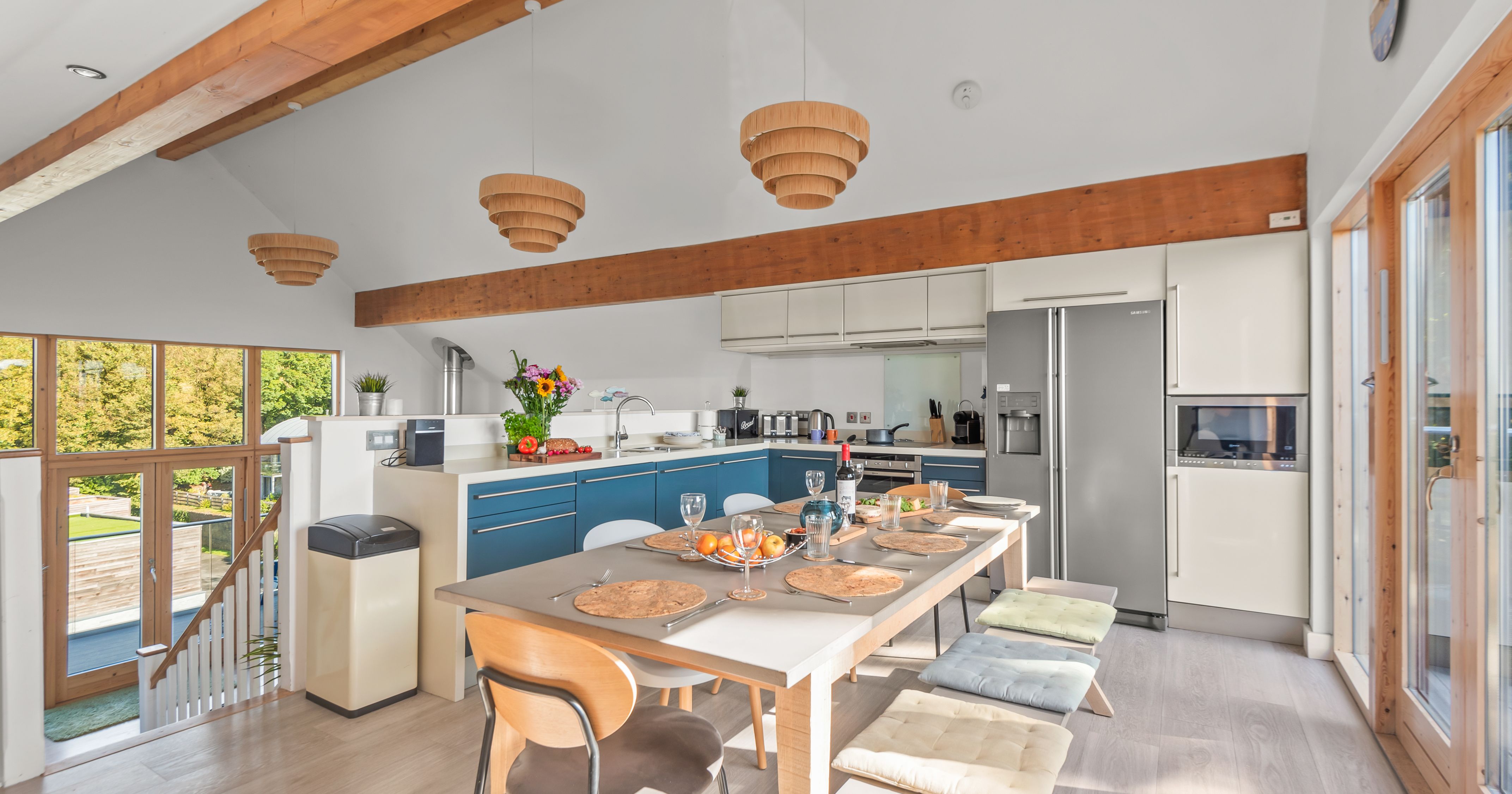 Modern kitchen and dining area with wooden beams, blue cabinets, and large windows.