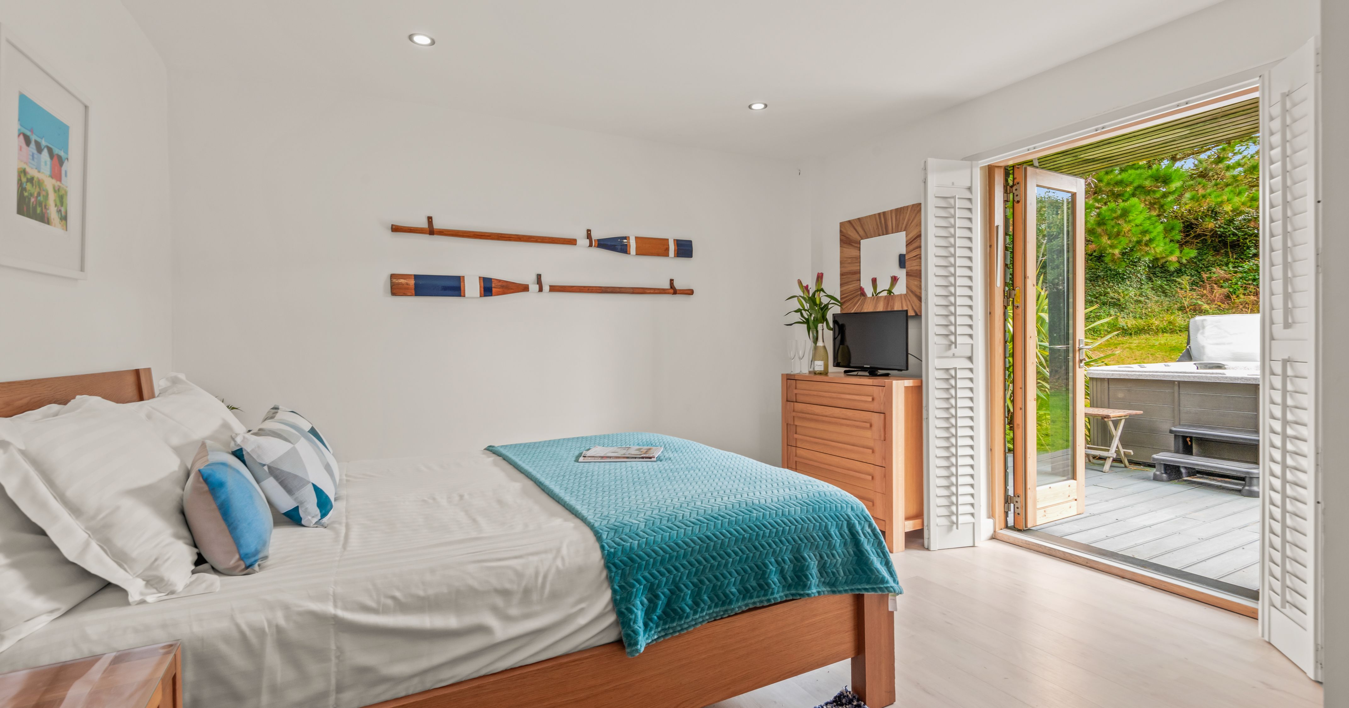 Bright bedroom with wooden furniture, nautical decor, and open doors to a patio with greenery.