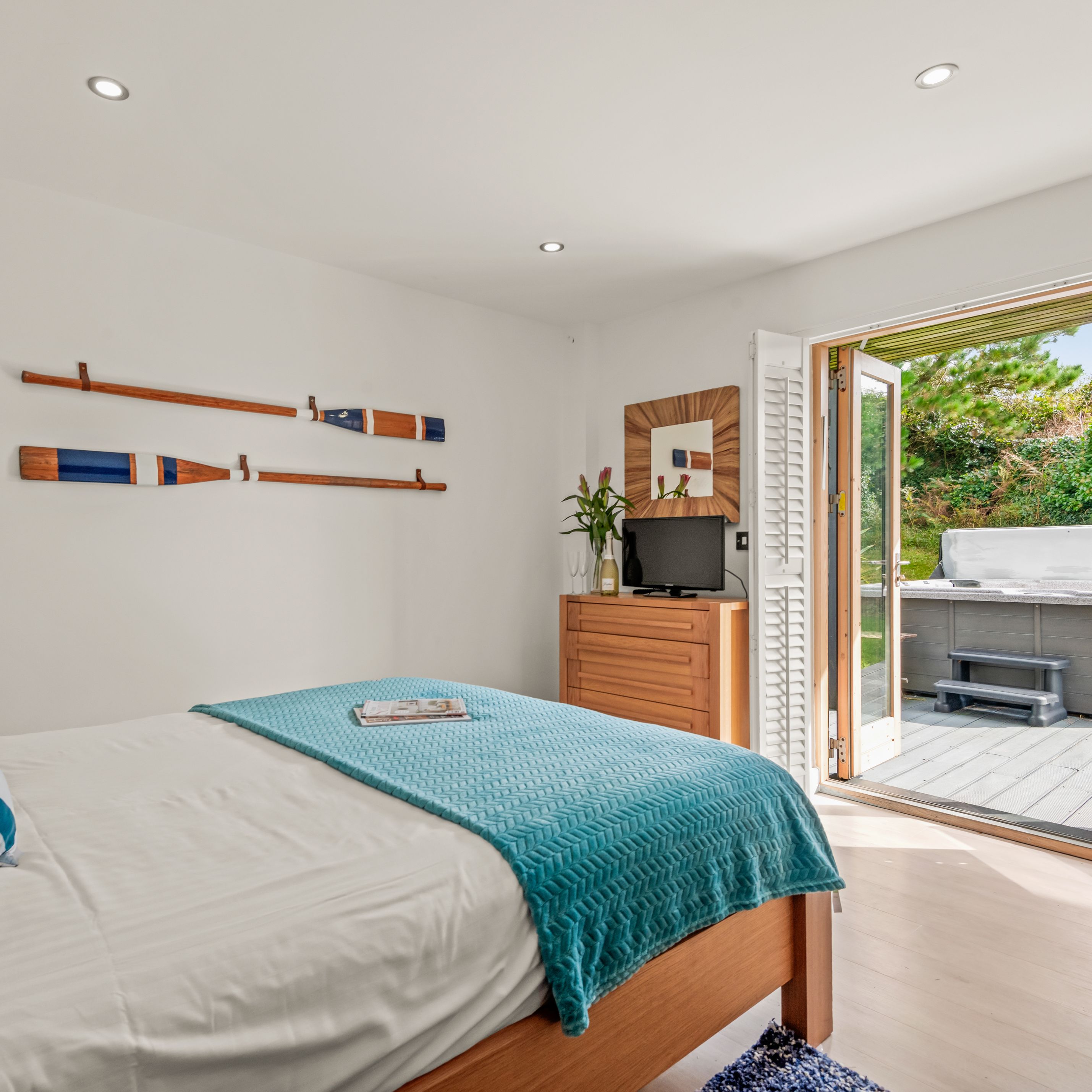 Bright bedroom with turquoise blanket and open doors leading to an outdoor hot tub