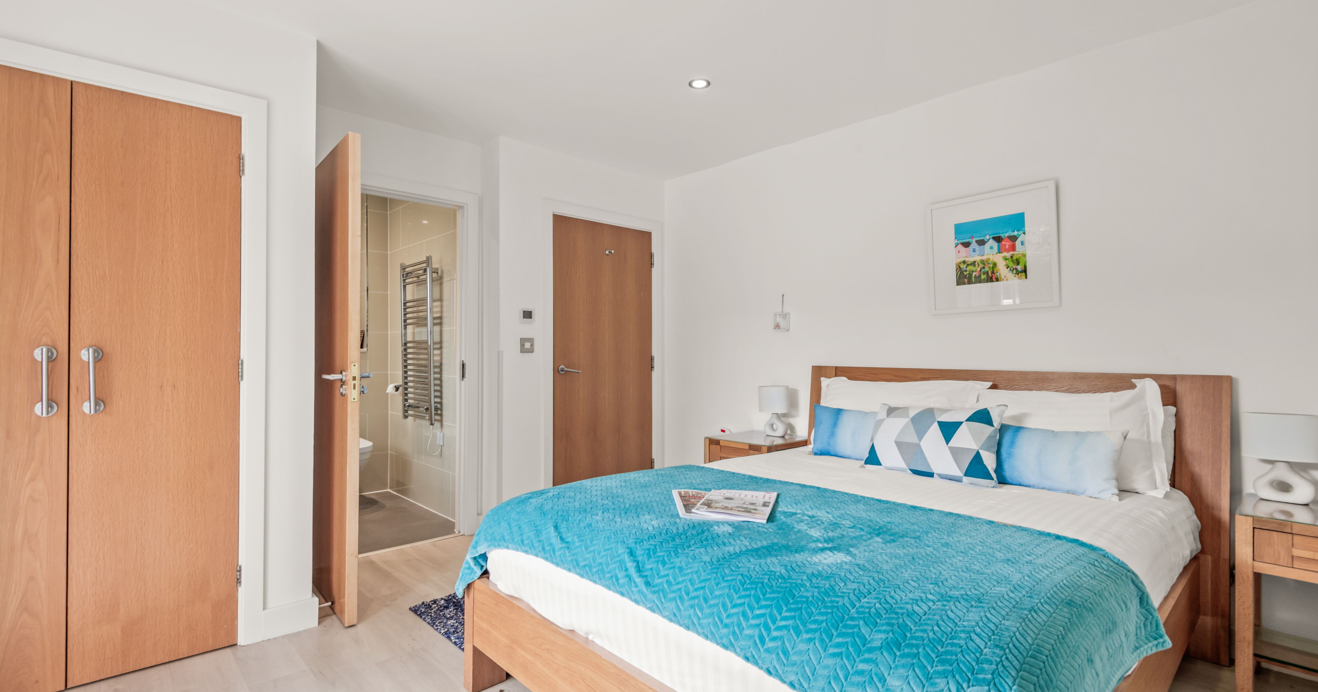 Modern bedroom with wooden furniture, blue bedding, and ensuite bathroom