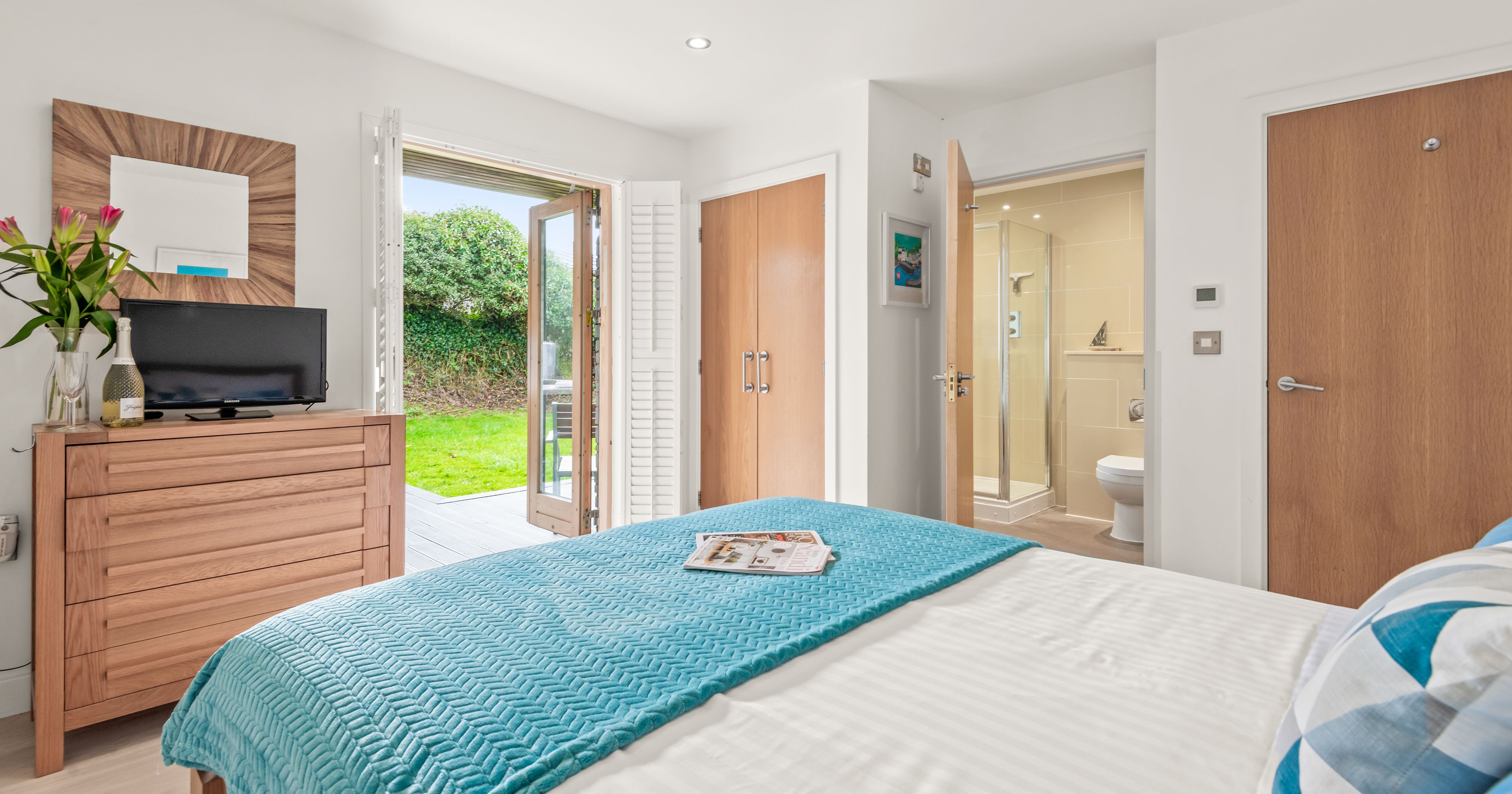 Modern bedroom with en-suite bathroom and open doors to a garden