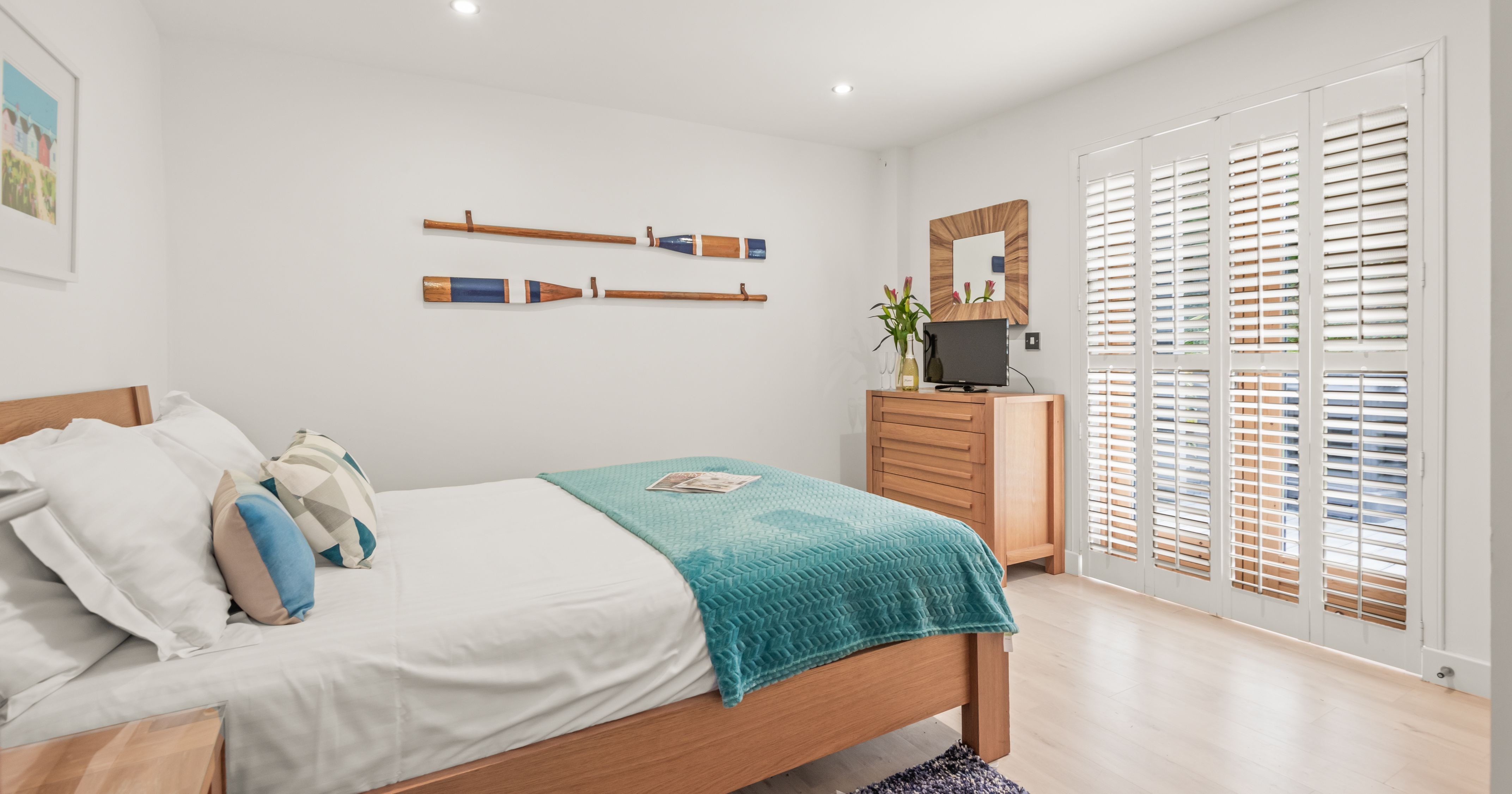 Modern bedroom with wooden furniture, teal blanket, and white walls.