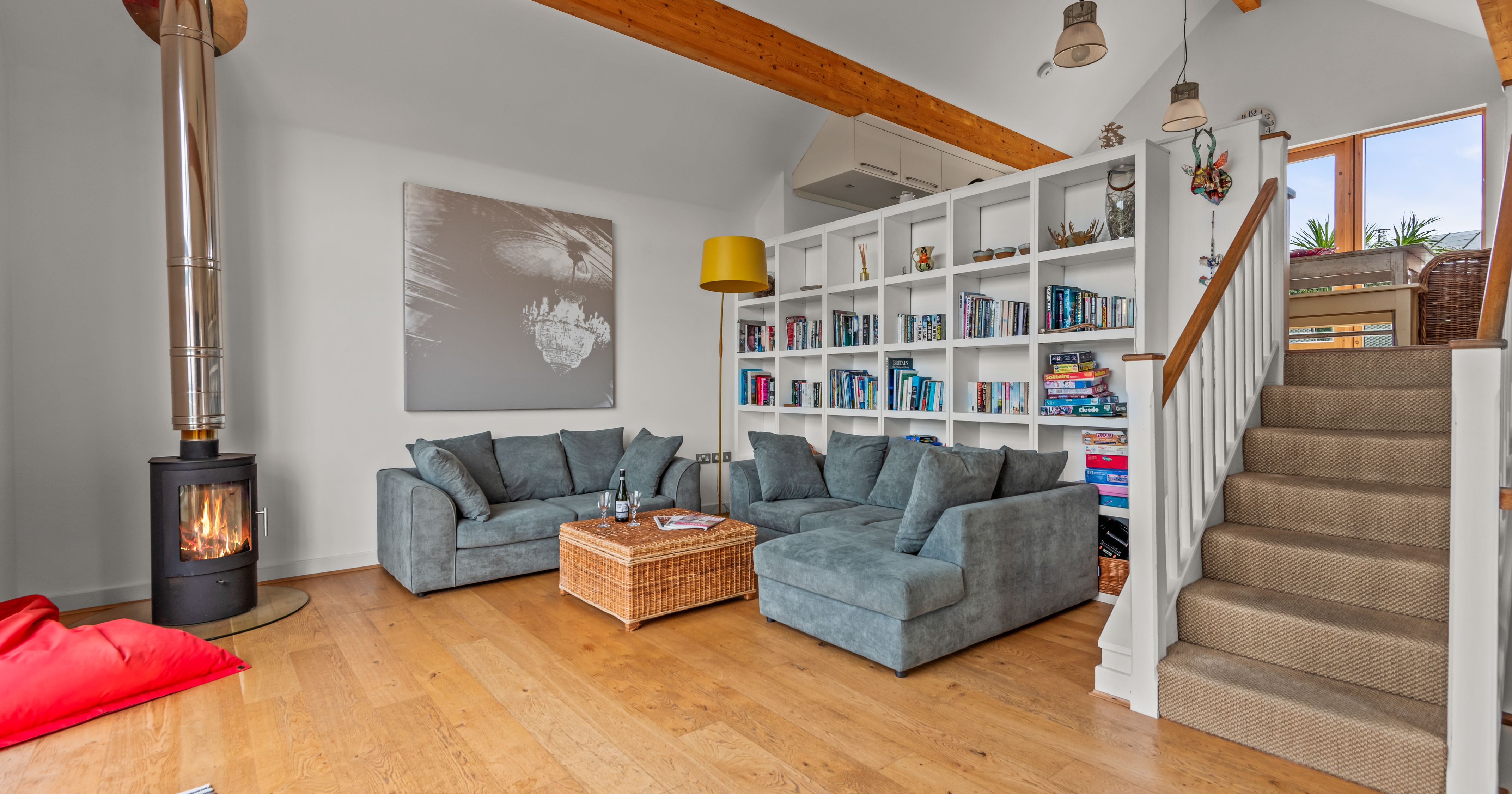 Modern living room with grey sofas, wood stove, bookshelf, and staircase