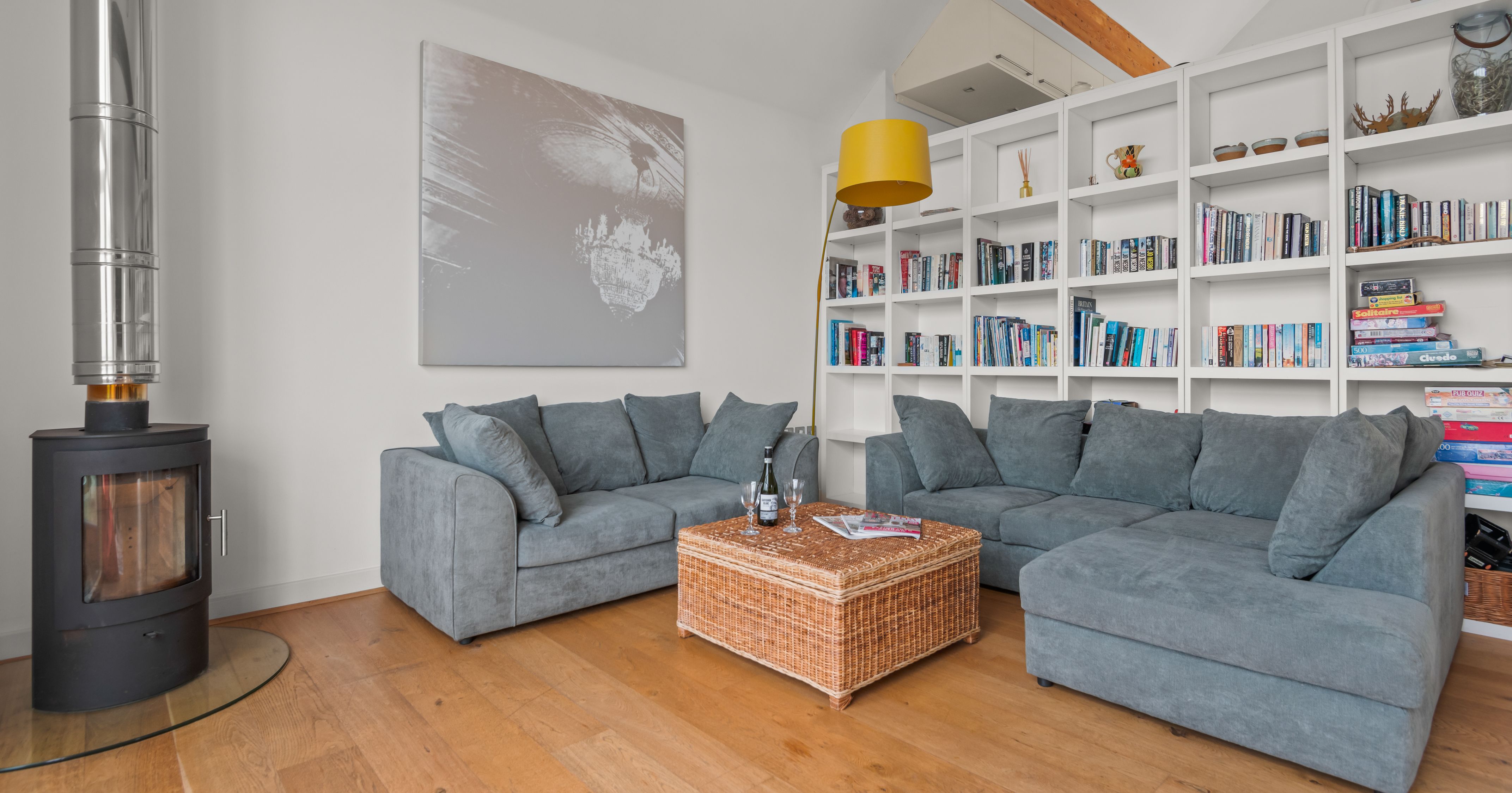 Modern living room with grey sectional sofas, a wood stove, bookshelf, and wicker coffee table