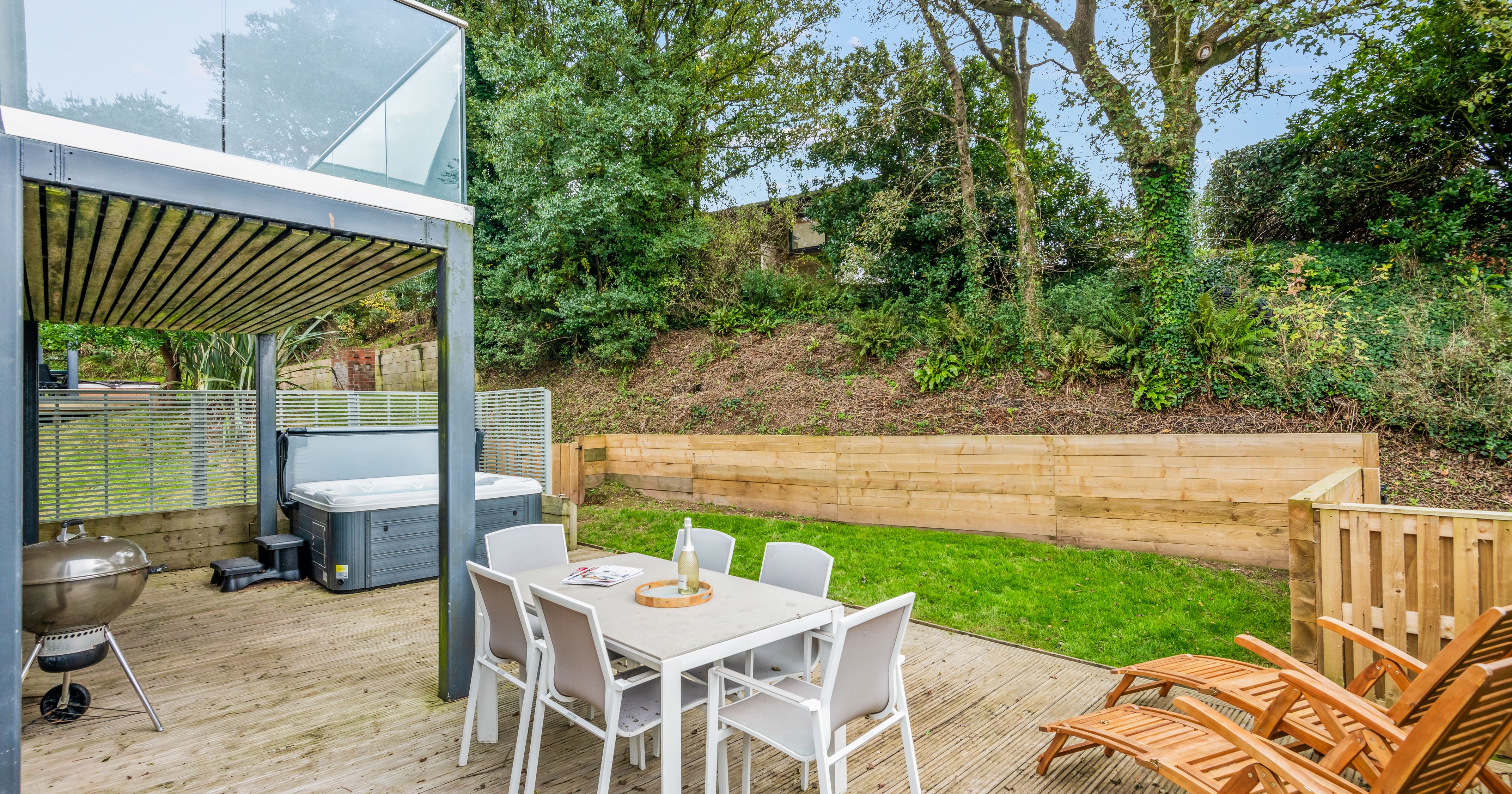 Modern outdoor patio with dining table, lounge chairs, hot tub, and green garden
