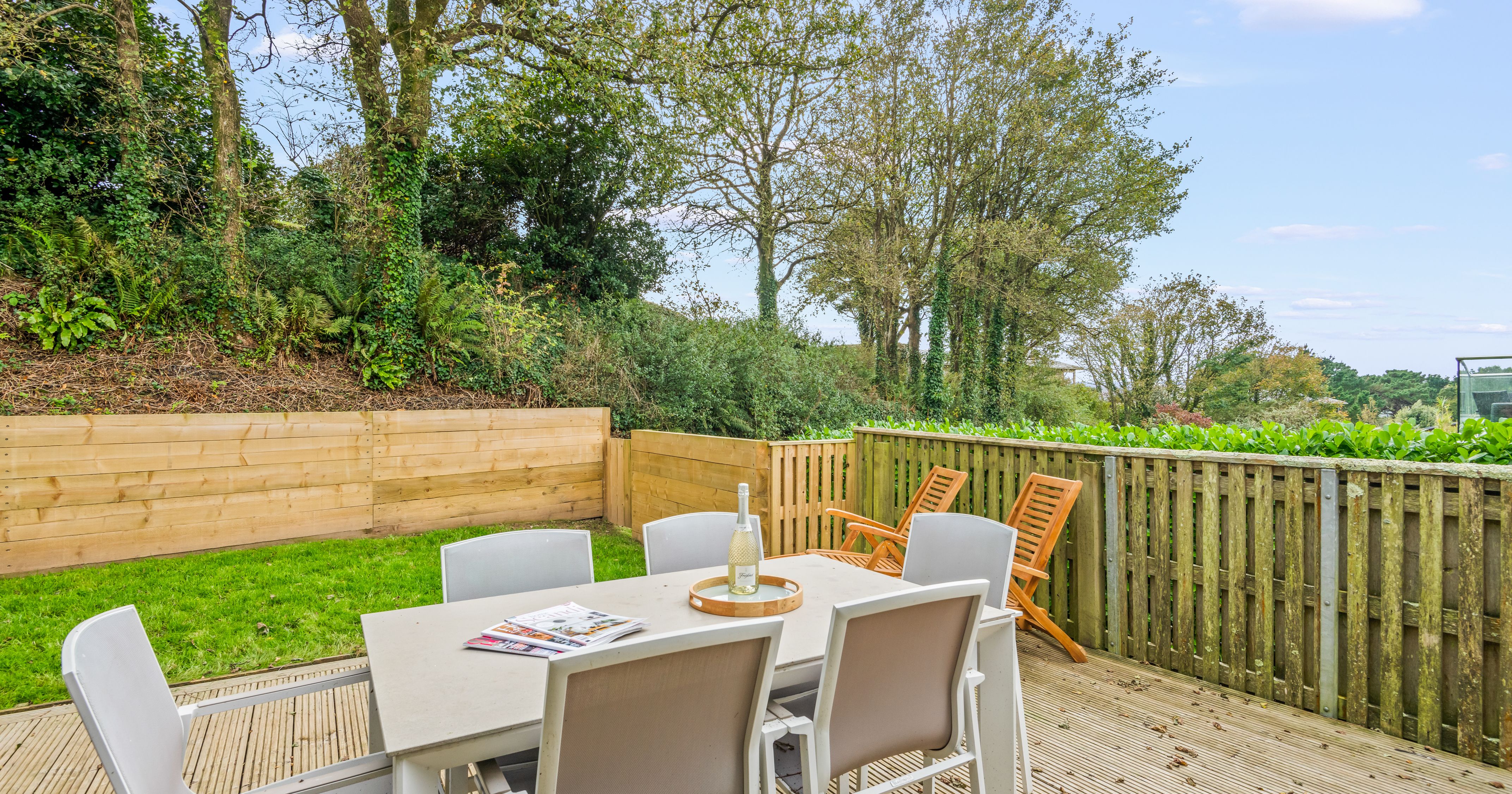 Outdoor patio area with table, chairs, and wooden fence overlooking greenery.