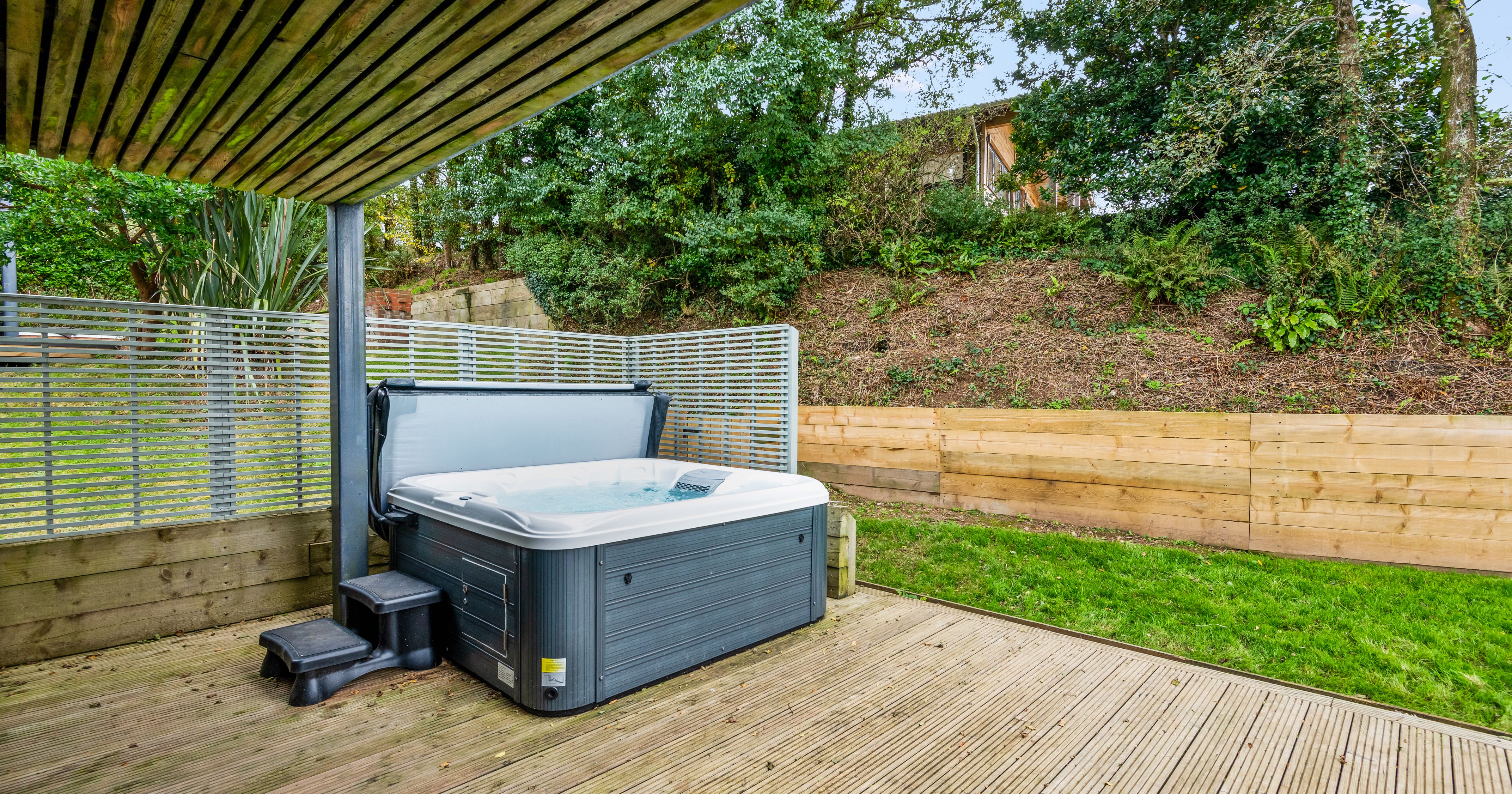 Outdoor hot tub on a wooden deck with steps, surrounded by a privacy screen and greenery.
