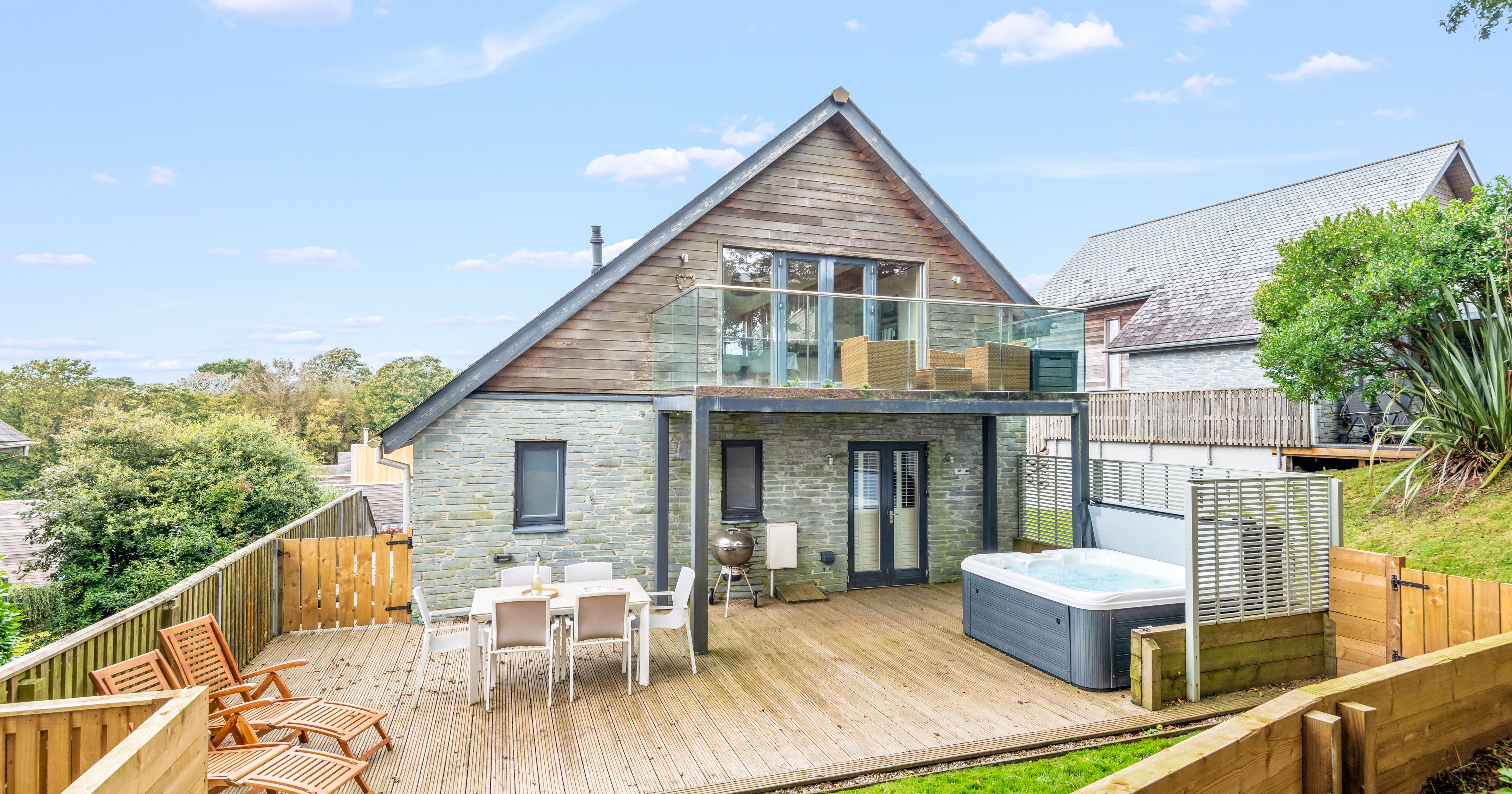 Modern house with stone and wood exterior, large deck, hot tub, outdoor dining area, and upper balcony.